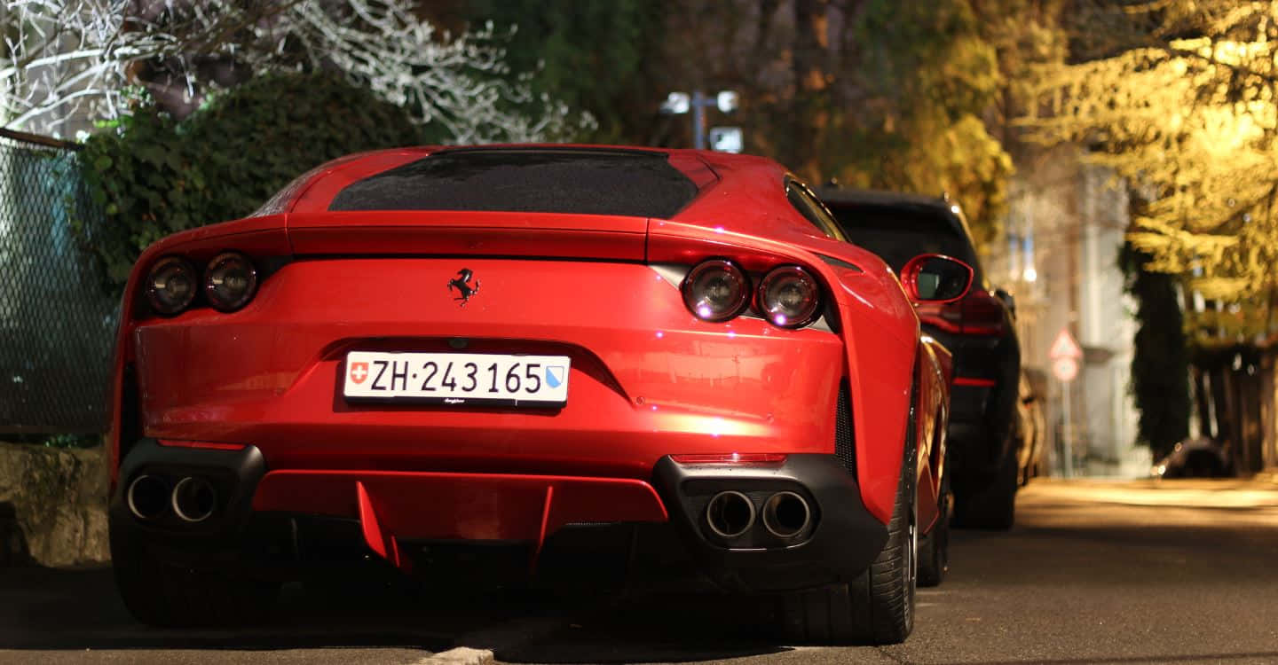 Ferrari 812 Superfast 桌布 壁紙 — 一輛鮮紅色的法拉利跑車在夜間停泊在綠樹成蔭的街道上，溫暖的路燈在其光澤表面投射出金色倒影。