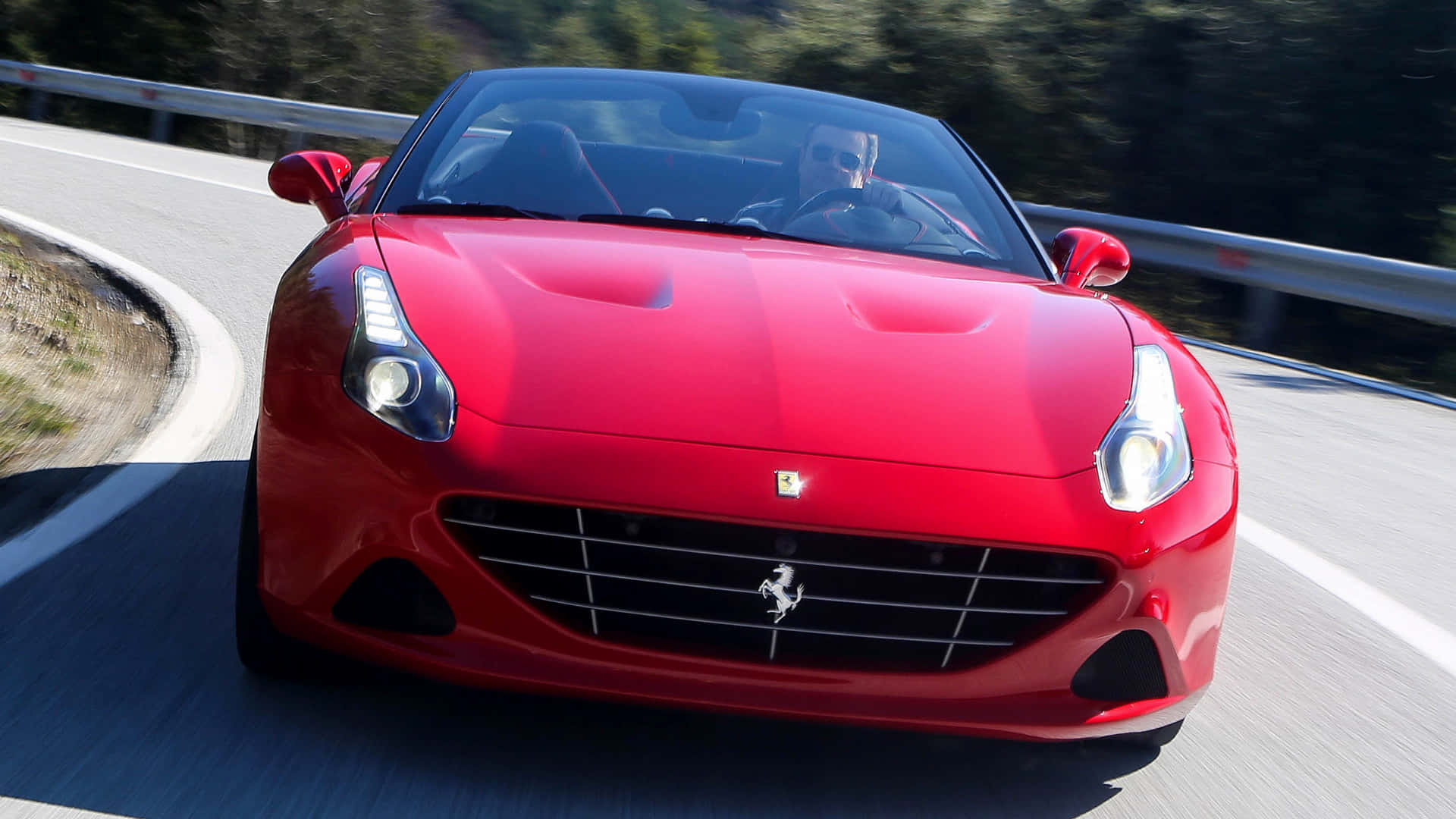 Ferrari California T 桌布 壁紙 — 一輛鮮紅色的法拉利跑車在蜿蜒的山路上疾馳，司機手握方向盤。