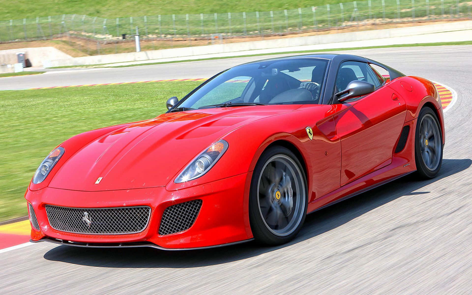 Ferrari 599 Gtb Fiorano 桌布 壁紙 — 一輛鮮紅色的法拉利跑車在賽道彎道高速飛馳，瀝青路面呈現動態模糊，遠方有綠草。