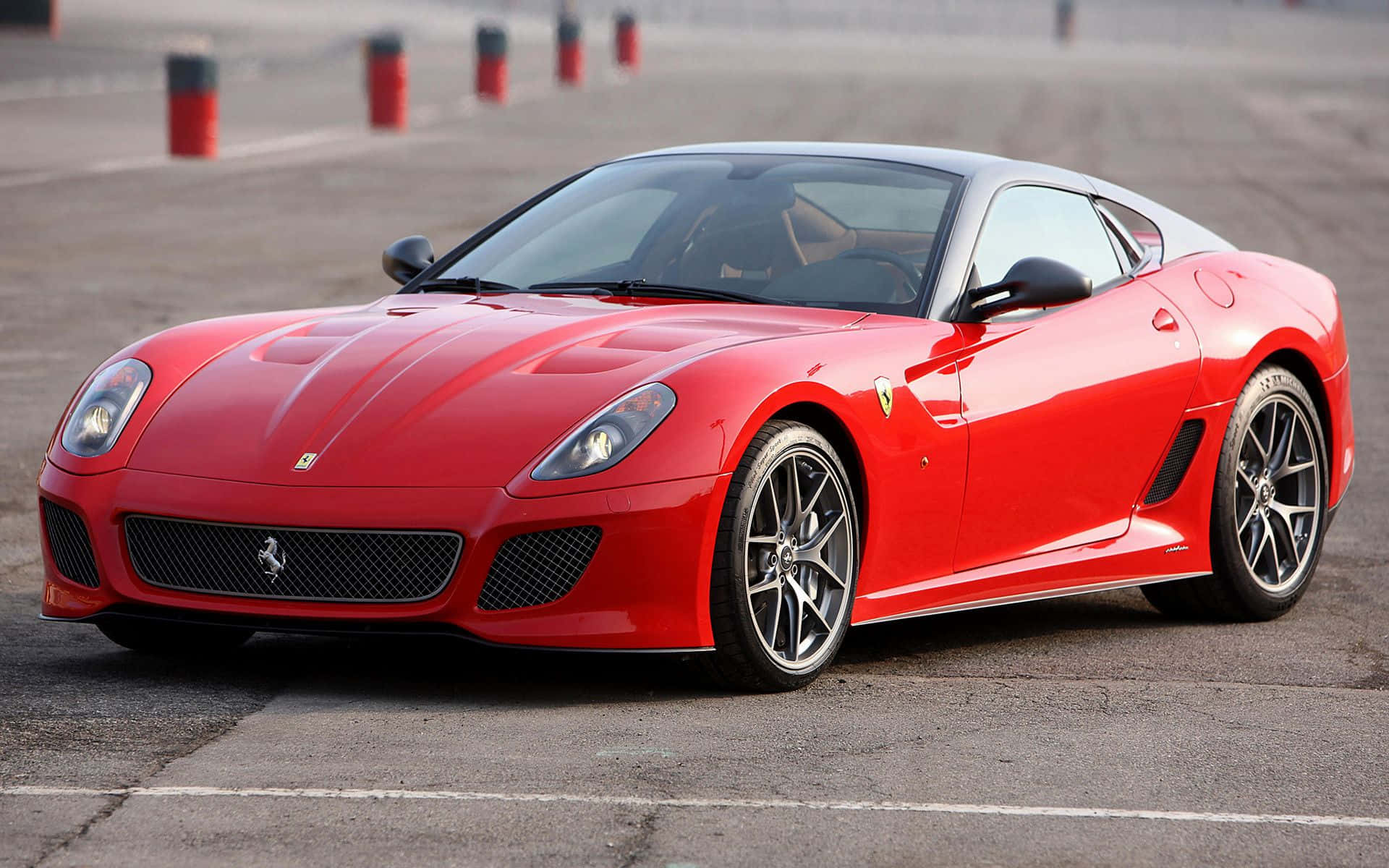 Ferrari 599 Gtb Fiorano 桌布 壁紙 — 一輛鮮紅色的法拉利跑車在鋪砌的賽道上閃閃發光，背景有紅色和黑色的障礙物。