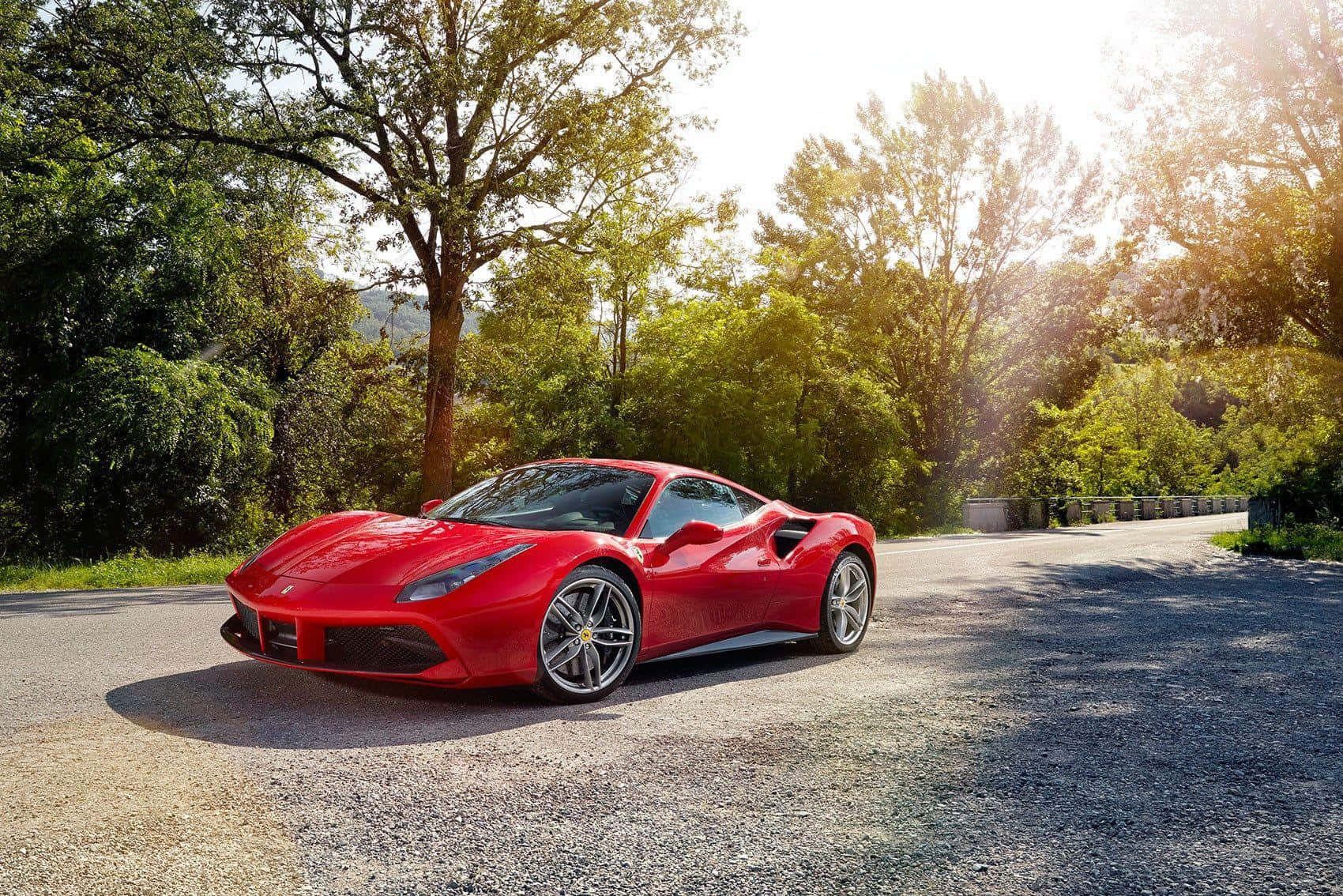 Ferrari 488 Spider 桌布 壁紙 — 一輛鮮紅色的法拉利跑車在陽光明媚的碎石路上閃閃發光，蜿蜒穿過茂密的綠樹。