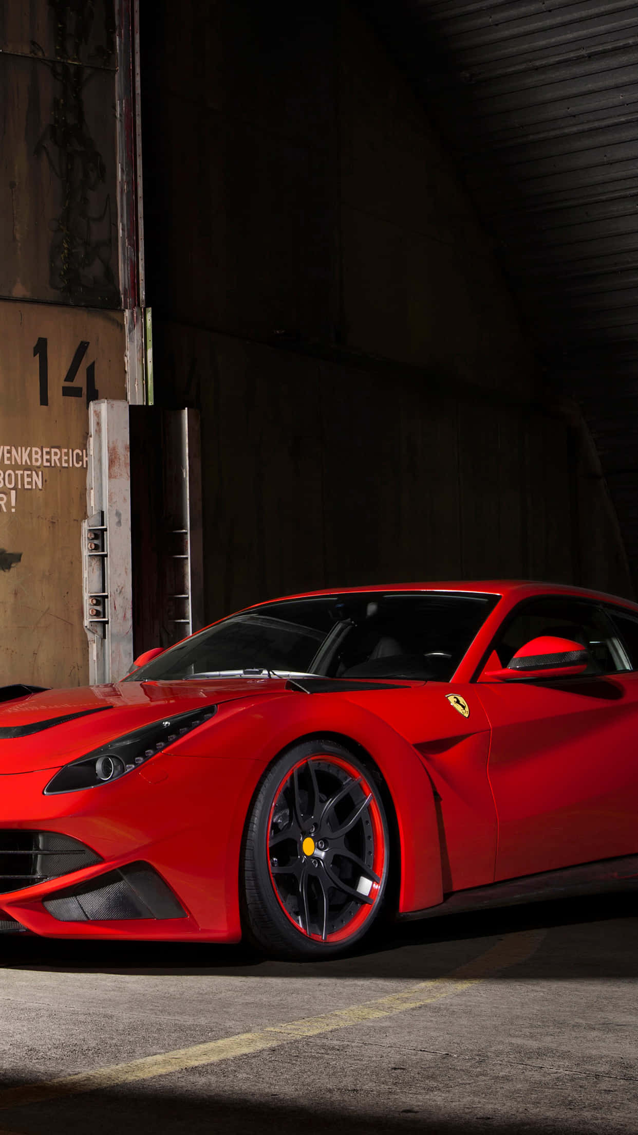 Ferrari iPhone 桌布 壁紙 — 一輛鮮紅色的法拉利跑車在骯髒的工業車庫內，在戲劇性的燈光下閃閃發光。