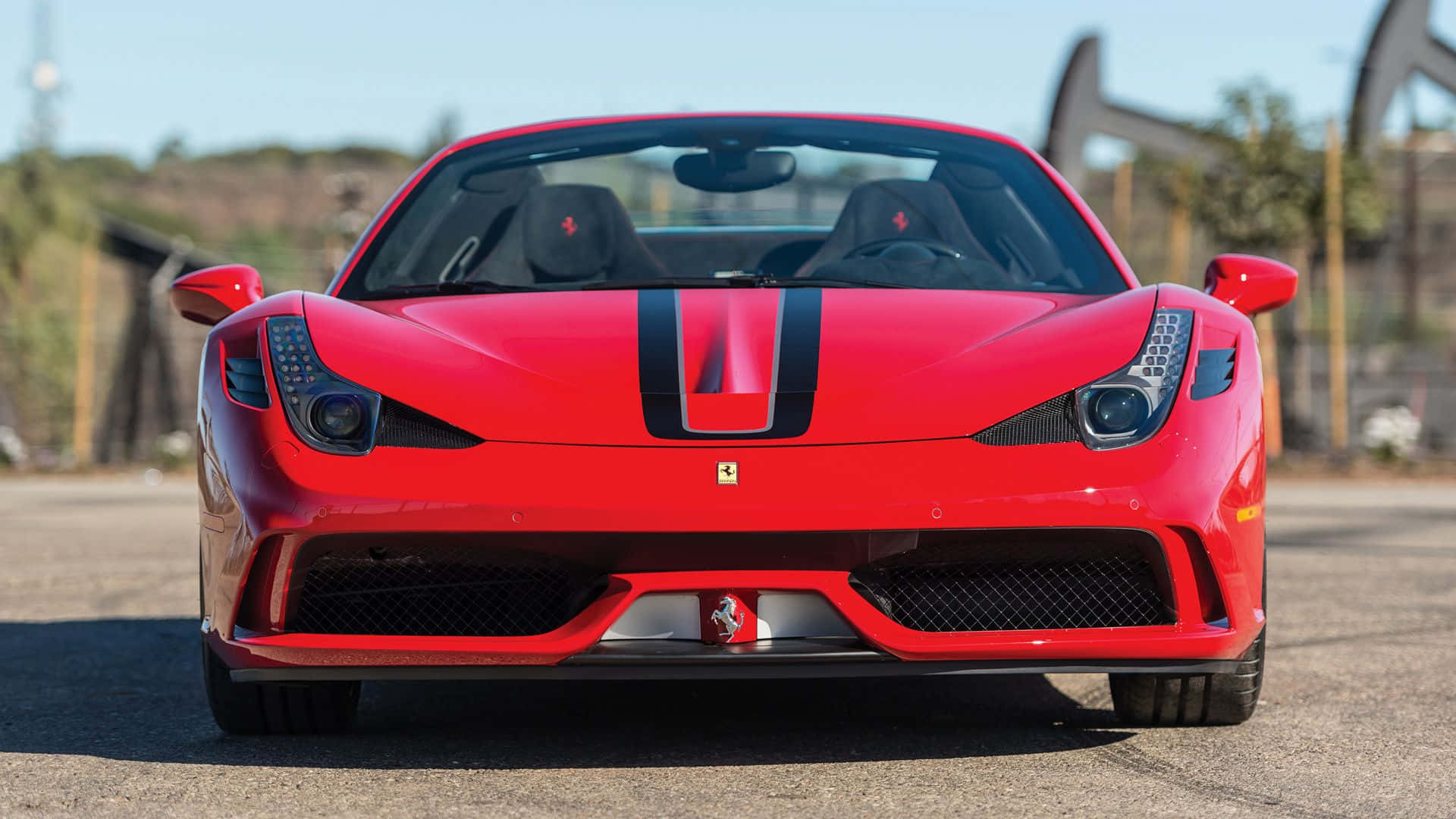 Ferrari 458 Speciale 桌布 壁紙 — 一輛鮮紅色的法拉利跑車帶有黑色賽車條紋，在陽光明媚的瀝青場地上正面朝前。