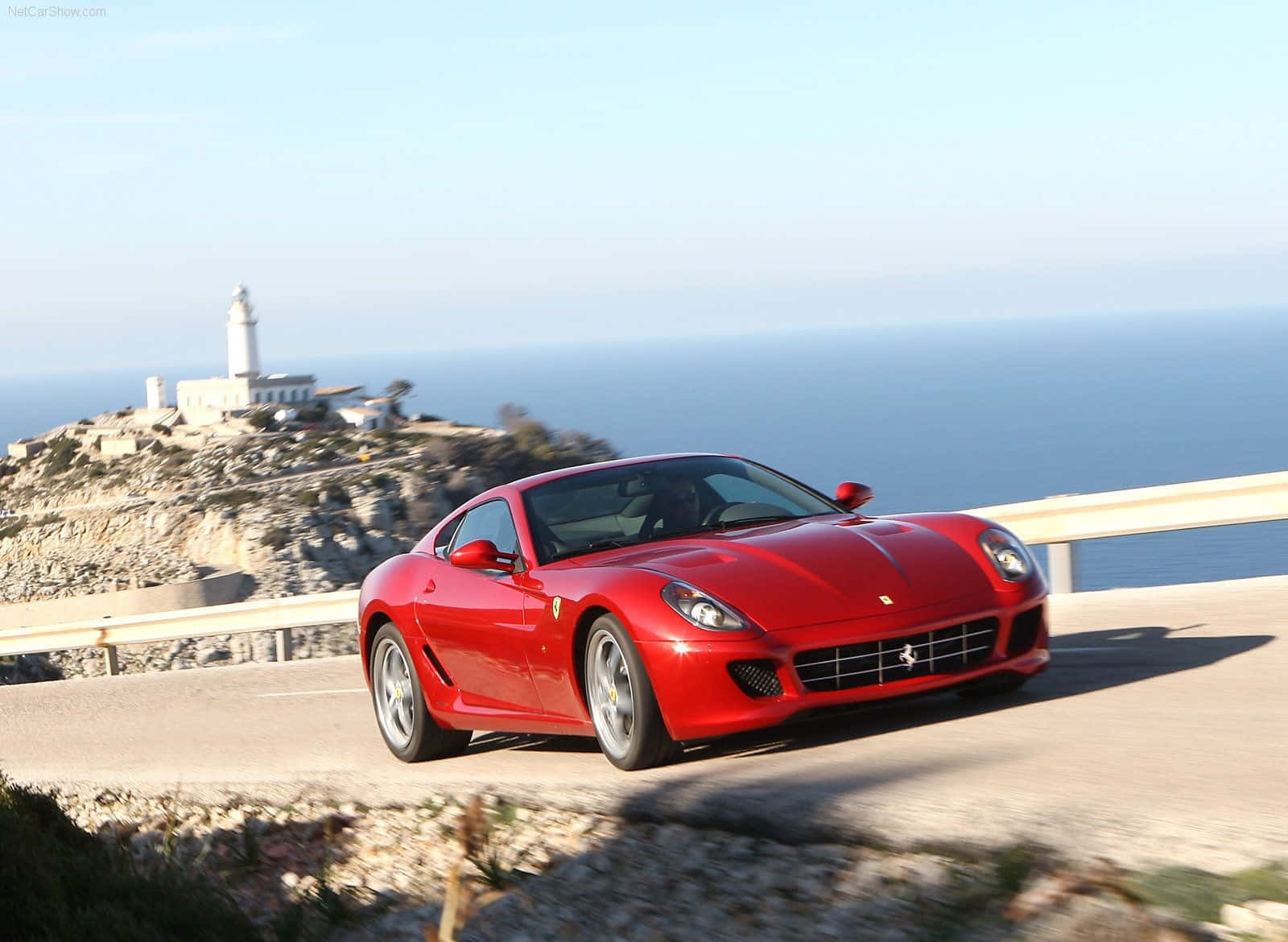 Ferrari 599 Gtb Fiorano 桌布 壁紙 — 一輛鮮紅色的法拉利跑車沿著海岸懸崖道路行駛，背景有燈塔和海洋。