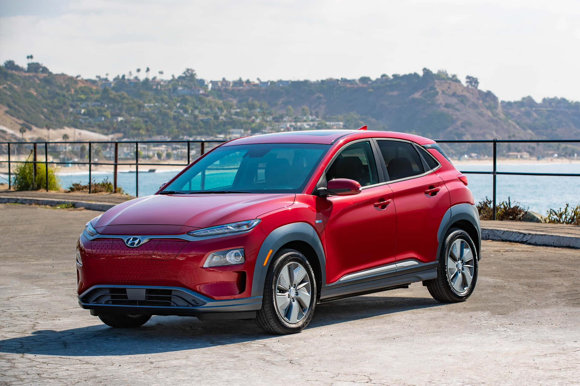 Hyundai 桌布 壁紙 — 一輛鮮紅色的現代Kona SUV停泊在海岸觀景點，背景是海洋和山丘。