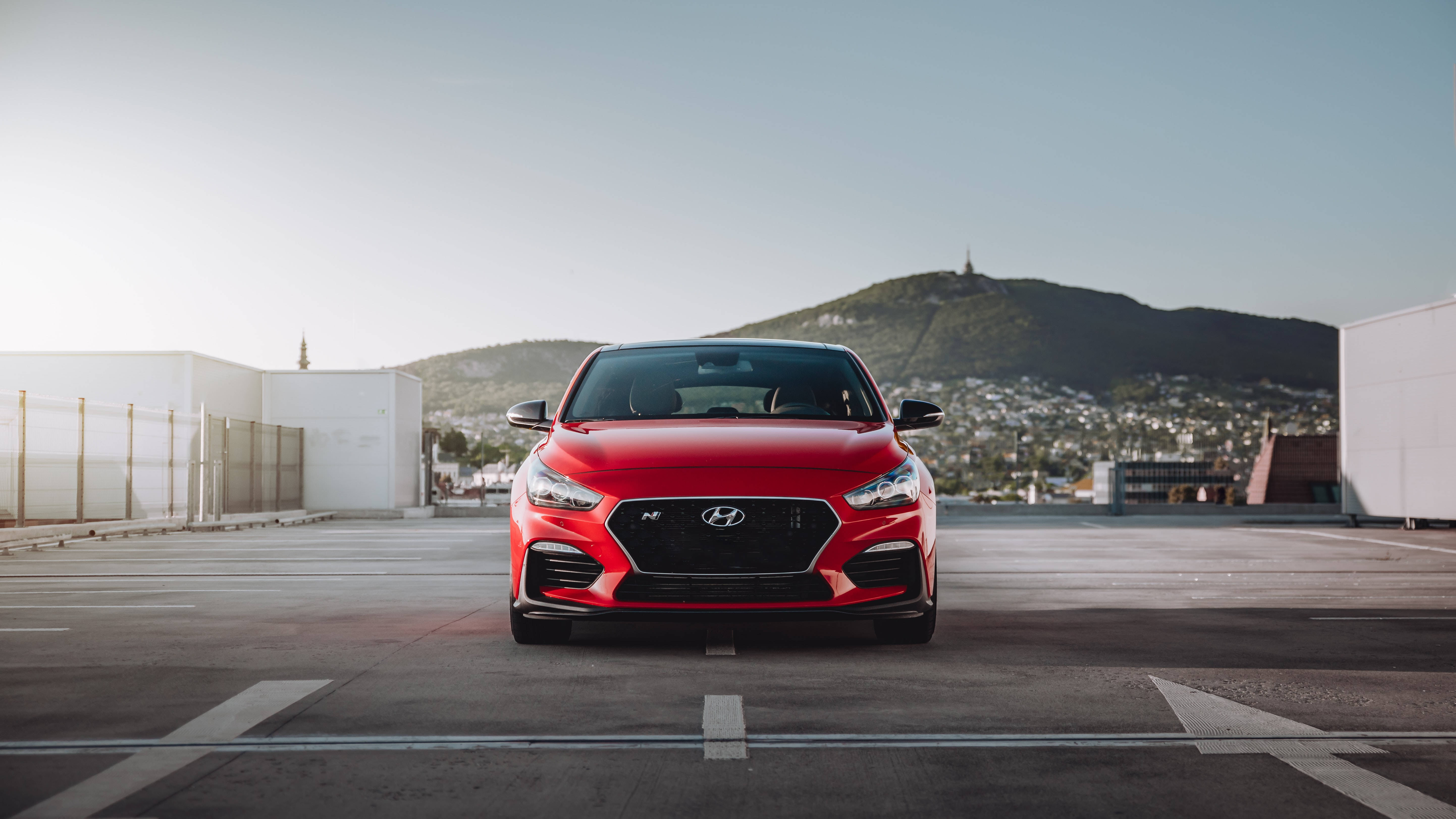 Hyundai 桌布 壁紙 — 一輛鮮紅色的現代跑車停放在屋頂上，背景是山脈和城市景觀，天空晴朗。