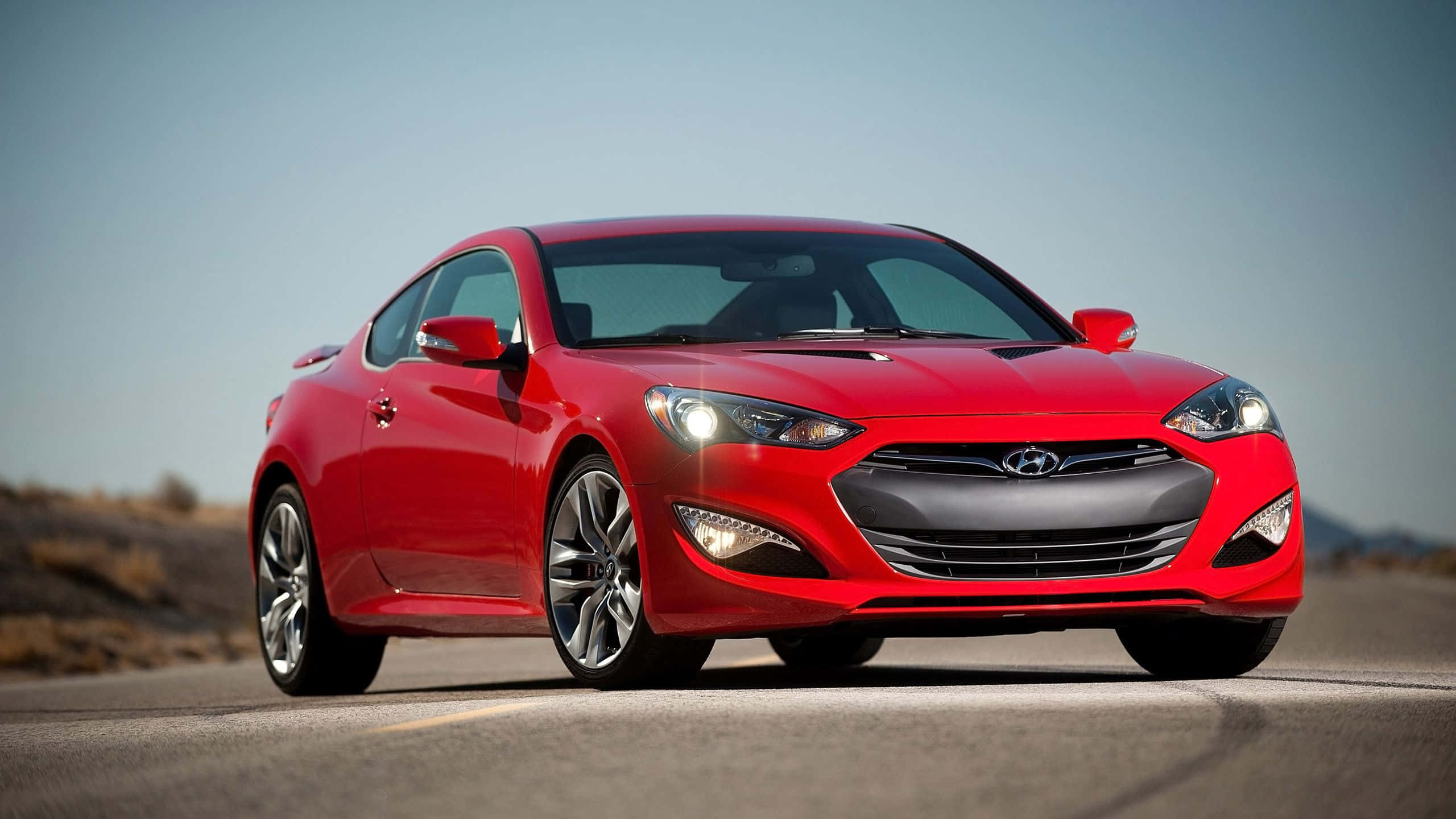 Hyundai Genesis 桌布 壁紙 — 一輛鮮紅色的現代運動型轎跑車在明亮的日光下閃閃發光，在沙漠公路上疾馳。