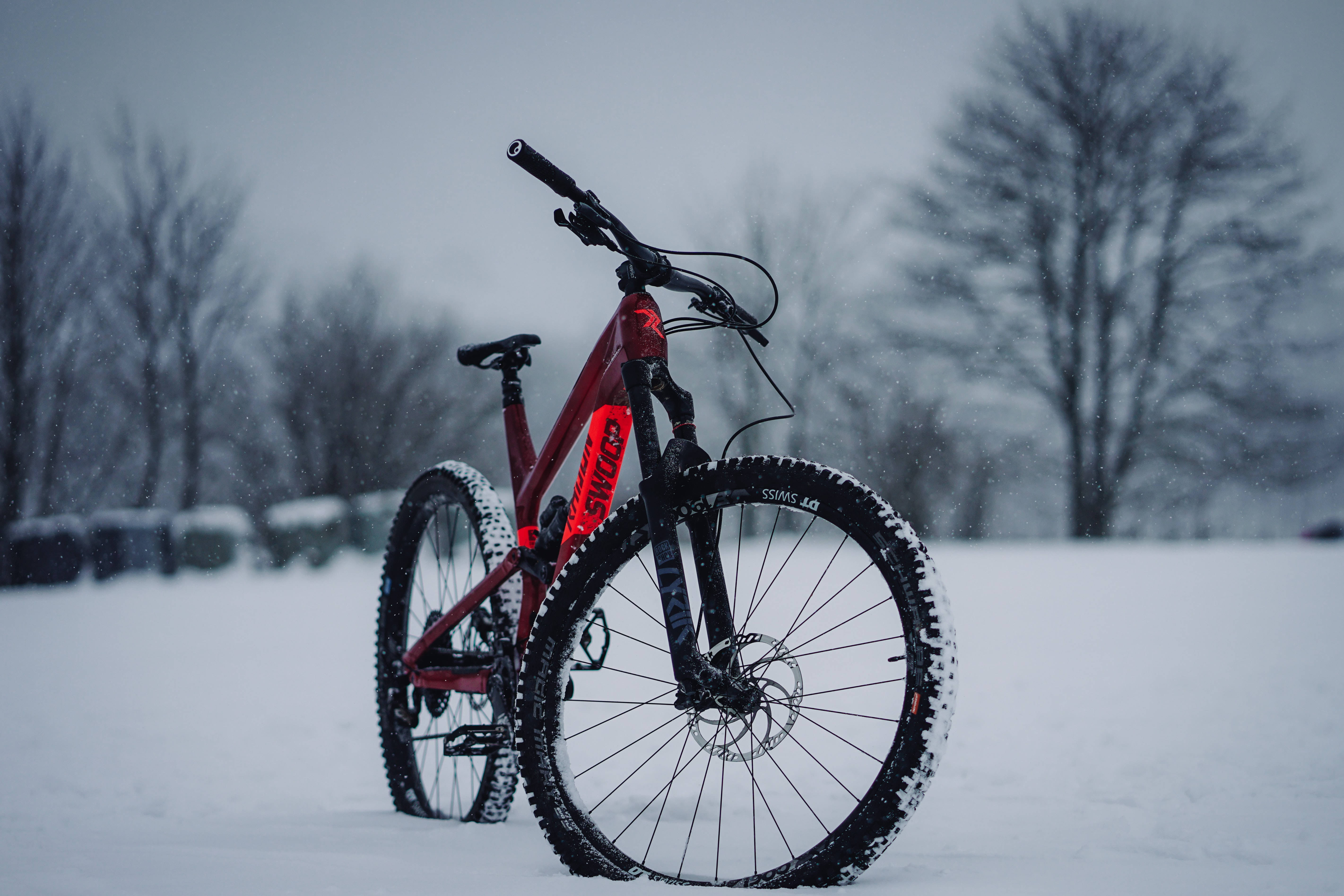 Mountain Bike 桌布 壁紙 — 一輛鮮紅色的登山自行車獨自站在雪地上，周圍是光禿禿的樹木，天空多雲。