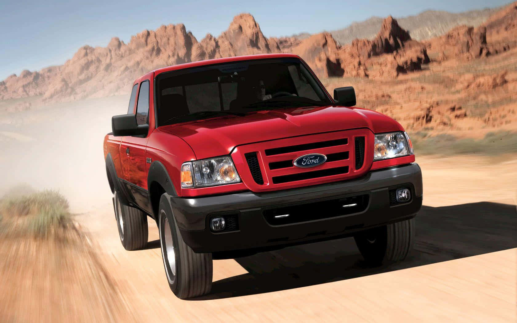 Ford Ranger 桌布 壁紙 — 一輛鮮紅色的福特 Ranger 皮卡車在塵土飛揚的沙漠道路上疾馳，背景是崎嶇的岩石地貌。