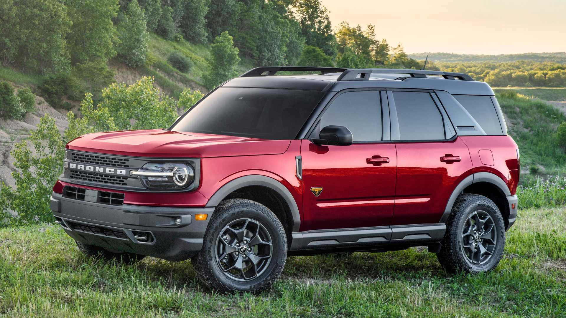 Ford Bronco 桌布 壁紙 — 一輛鮮紅色的福特Bronco SUV矗立在草地上，樹木和遠山沐浴在金色的日落光芒中。