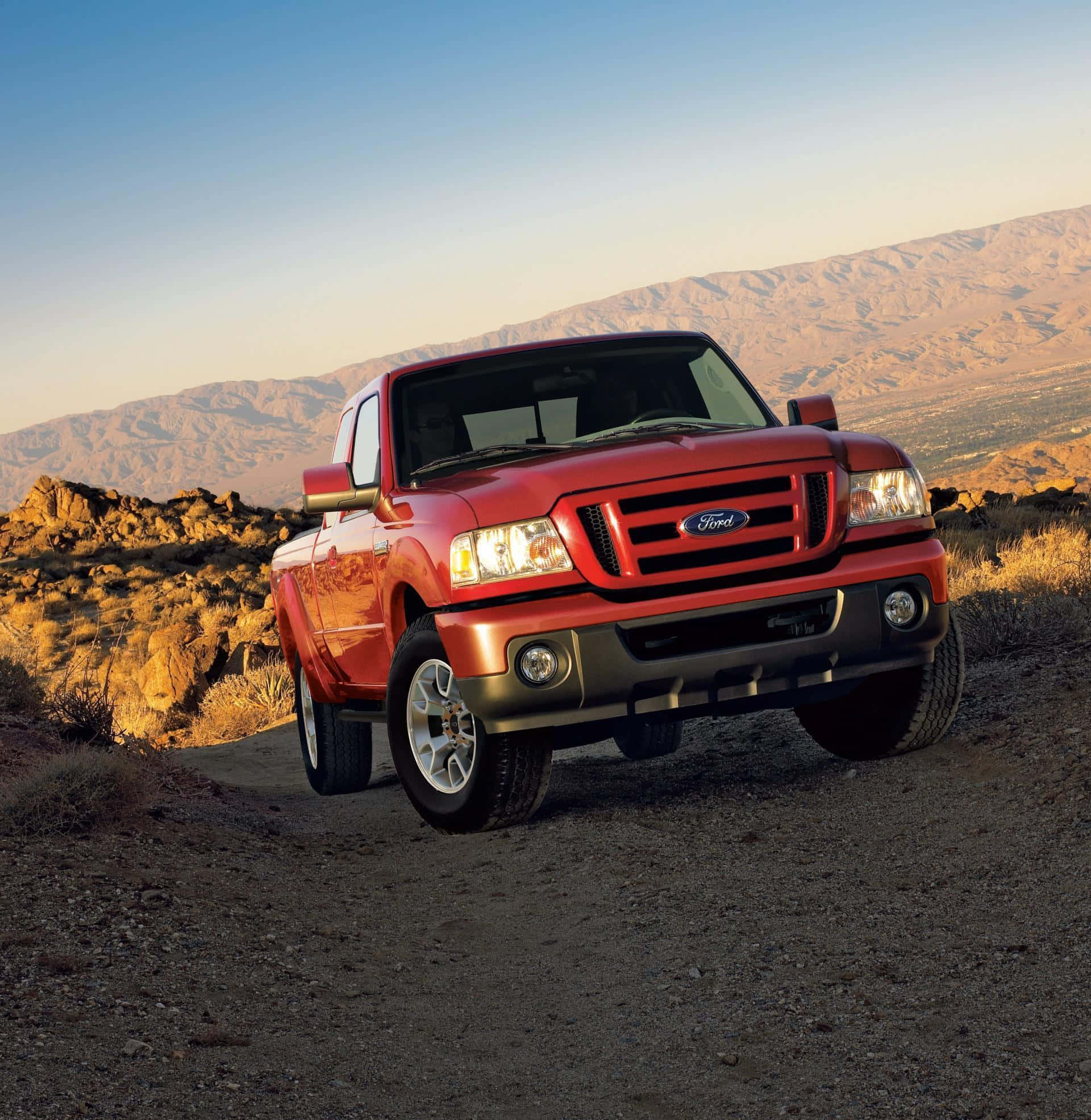 Ford Ranger 桌布 壁紙 — 一輛鮮紅色的福特皮卡車停在塵土飛揚的小徑上，崎嶇的山脈沐浴在金色的日落光芒中。