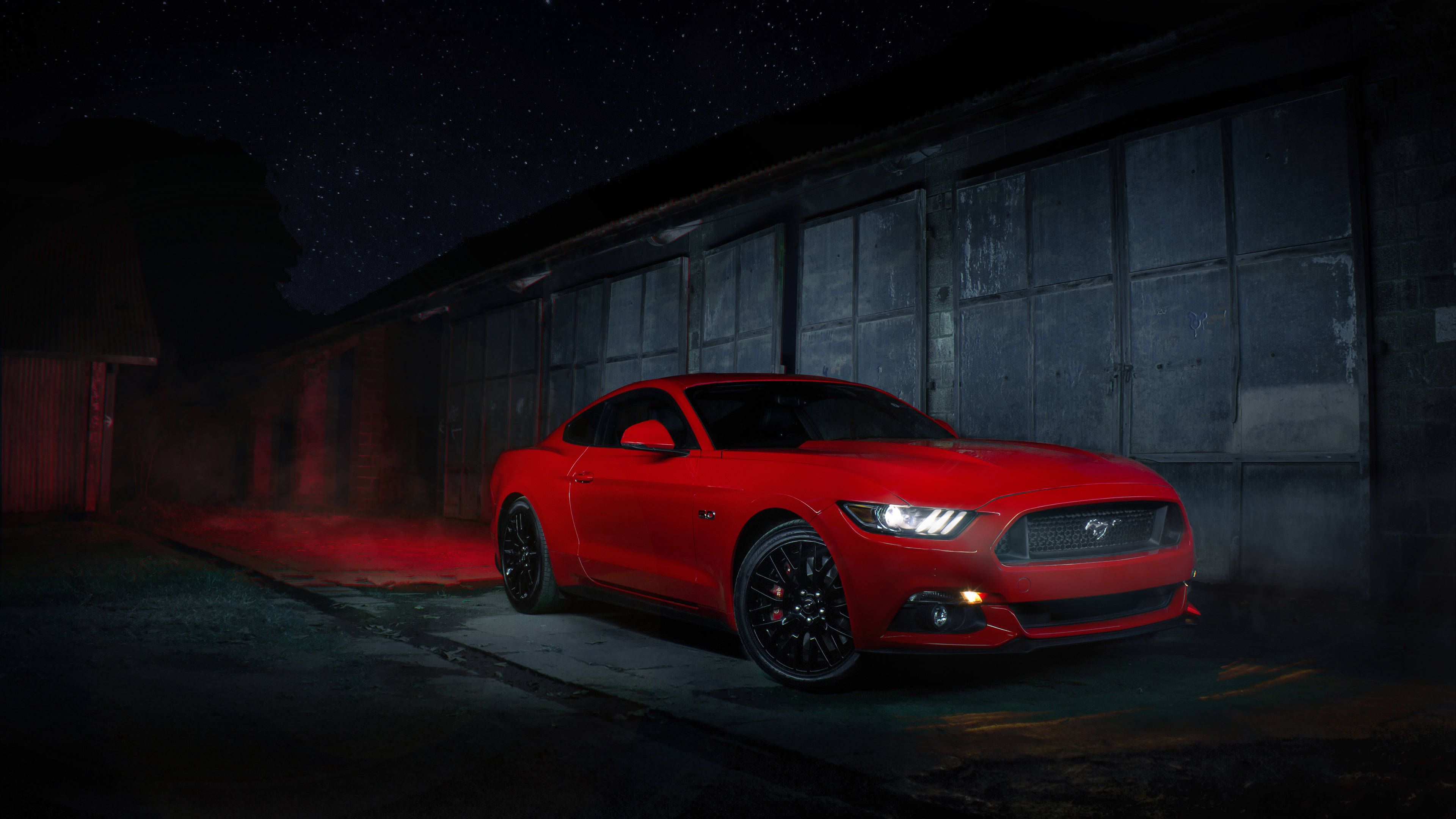 Cool Mustang 桌布 壁紙 — 一輛鮮紅色的福特野馬跑車在繁星點點的夜空下，在一座風化的工業建築旁閃耀。