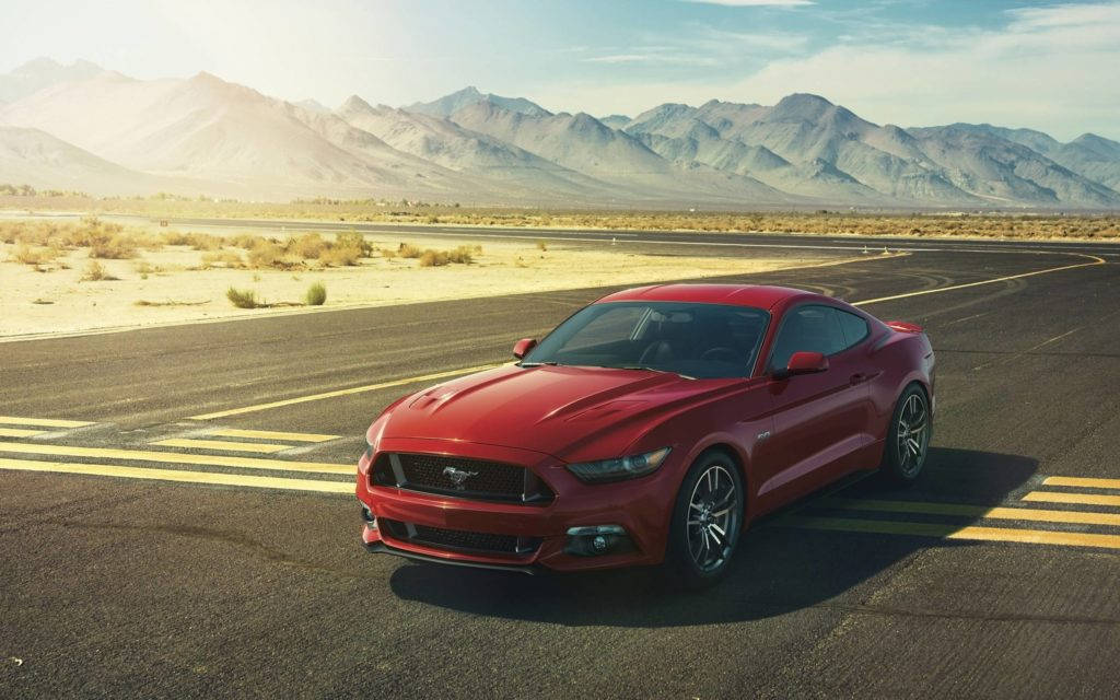 mustang HD 桌布 壁紙 — 一輛鮮紅色的福特野馬雙門跑車停在沙漠公路上，背景是崎嶇的山脈，天空晴朗蔚藍。