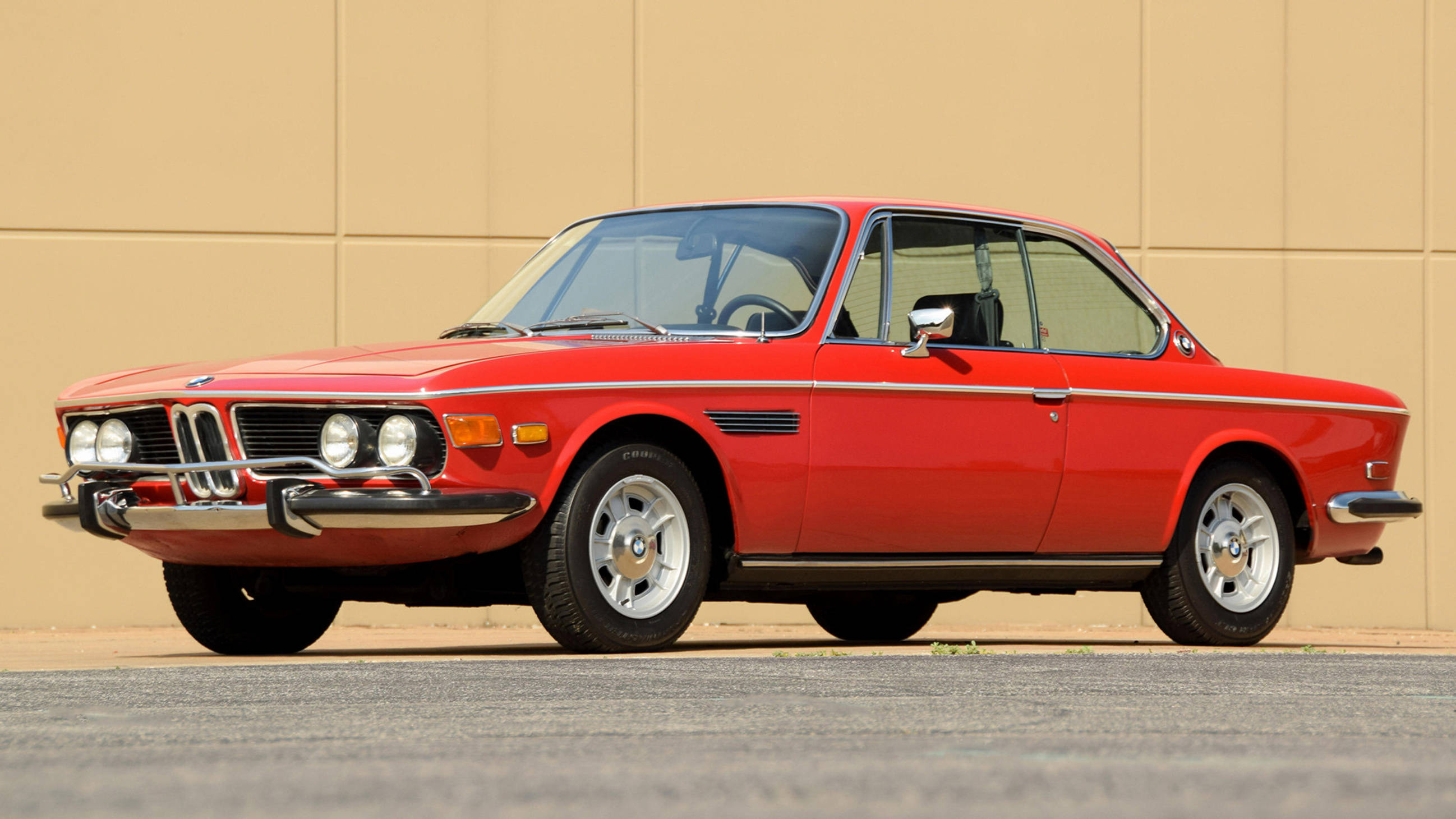 classic bmw 桌布 壁紙 — 一輛鮮紅色的經典BMW雙門轎跑車停在瀝青路上，背景是米色牆壁，在明亮的日光下。