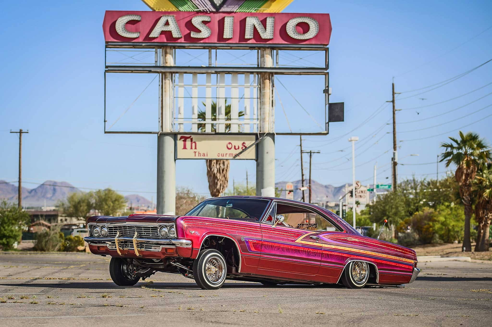 Lowrider 桌布 壁紙 — 一輛鮮紅色的經典低底盤汽車停在沙漠停車場一個褪色的賭場招牌下。