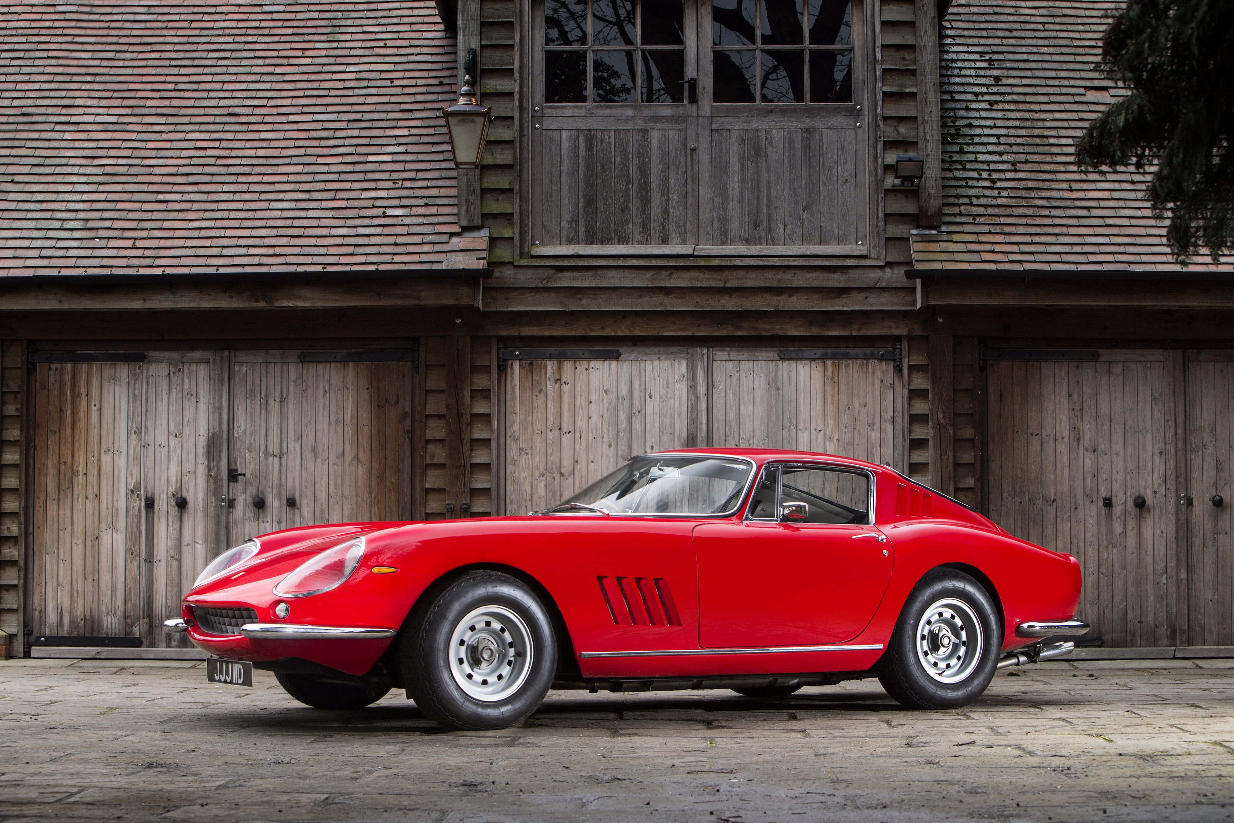 Vintage Ferrari 桌布 壁紙 — 一輛鮮紅色的經典法拉利275 GTB停放在一個質樸的木製穀倉前，穀倉有木瓦屋頂。