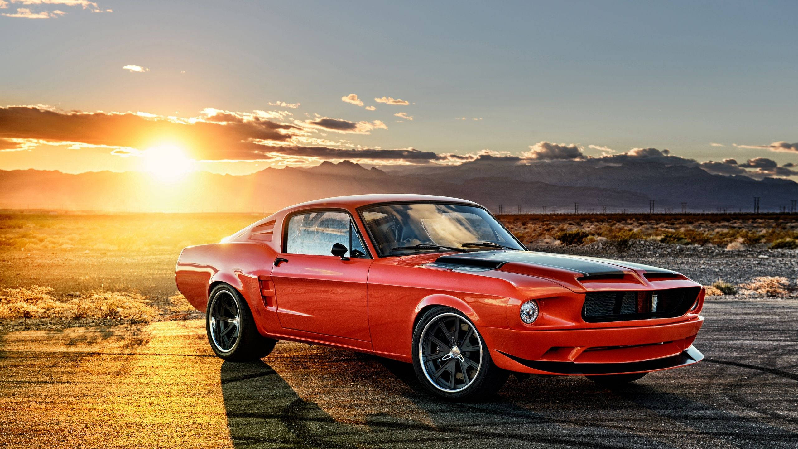Ford Mustang 桌布 壁紙 — 一輛鮮紅色的經典肌肉車在金色夕陽下閃耀，背景是沙漠景觀和遠處的山脈。