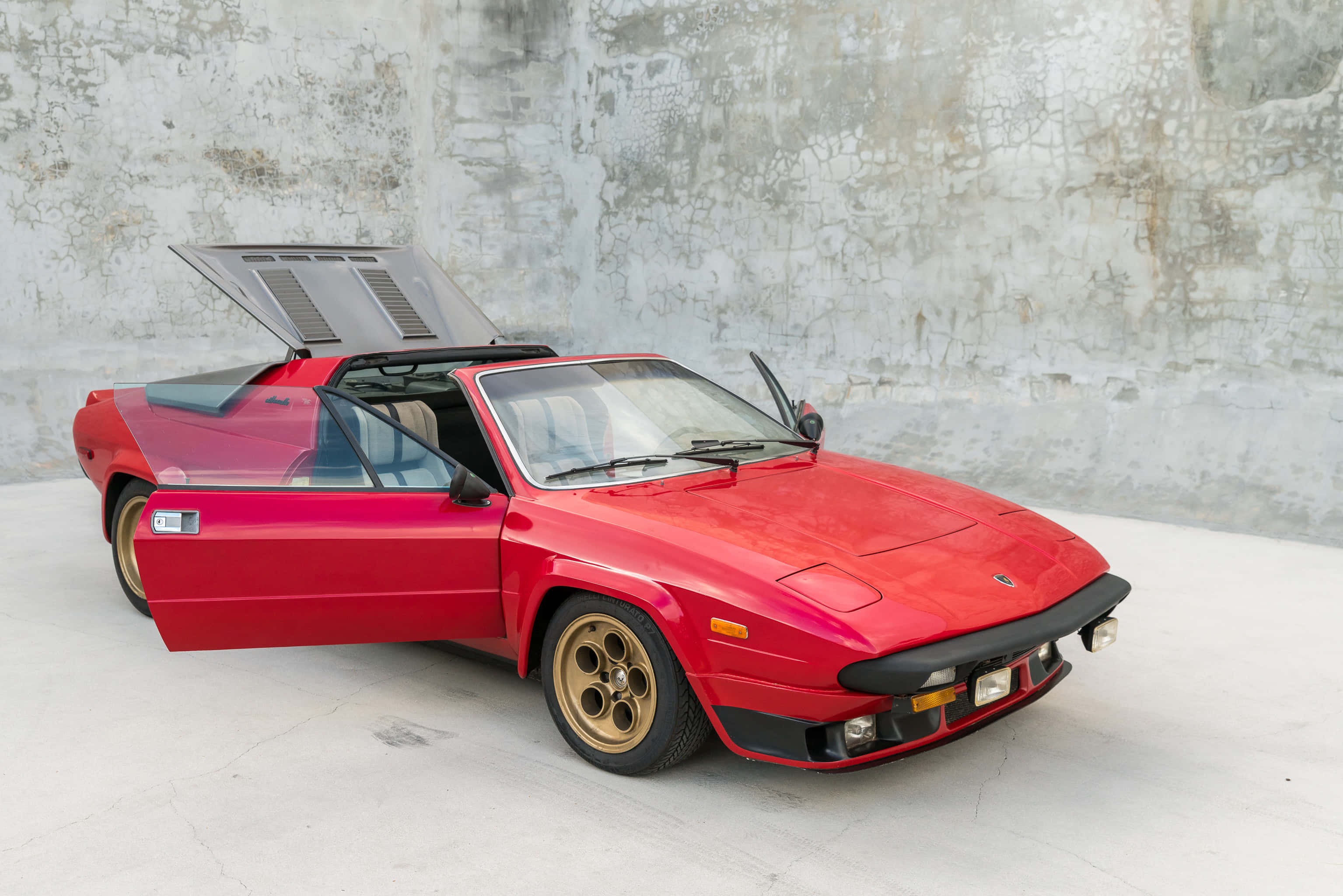 Lamborghini Silhouette 桌布 壁紙 — 一輛鮮紅色的經典跑車，鷗翼車門敞開，停在風化的混凝土牆前。