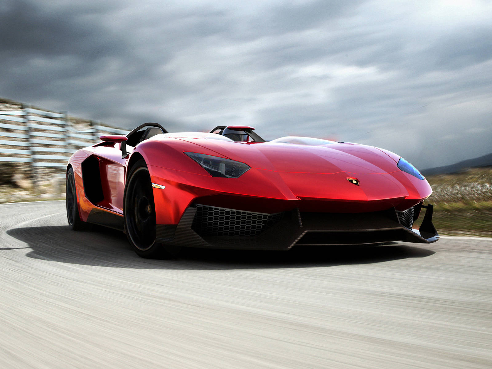 4K Lamborghini 桌布 壁紙 — 一輛鮮紅色的藍寶堅尼 Aventador Roadster 在戲劇性的多雲天空下沿著蜿蜒的道路疾馳。