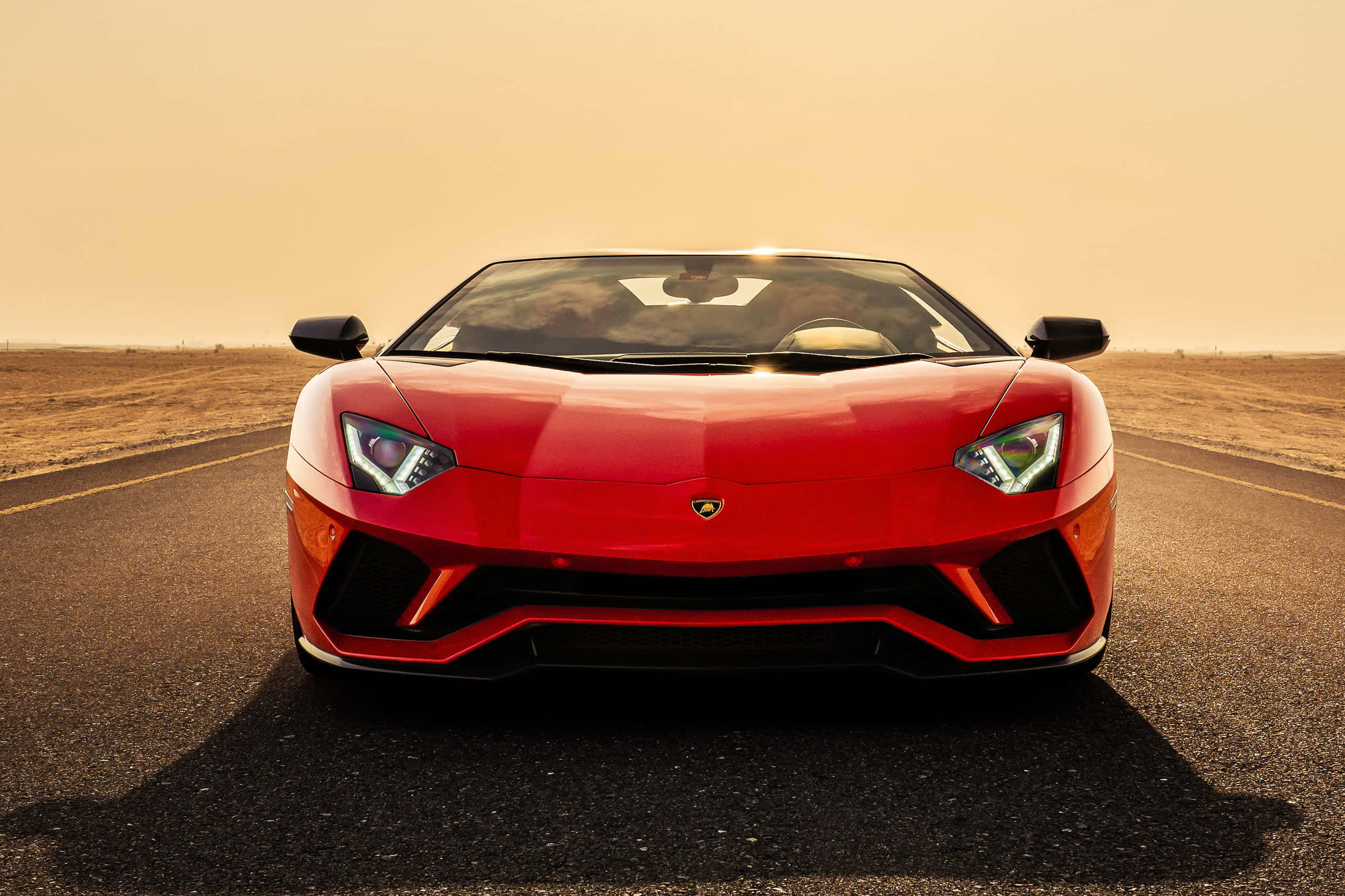 酷車 桌布 壁紙 — 一輛鮮紅色的藍寶堅尼 Aventador SVJ 在金色日落天空下的沙漠道路上向前行駛。