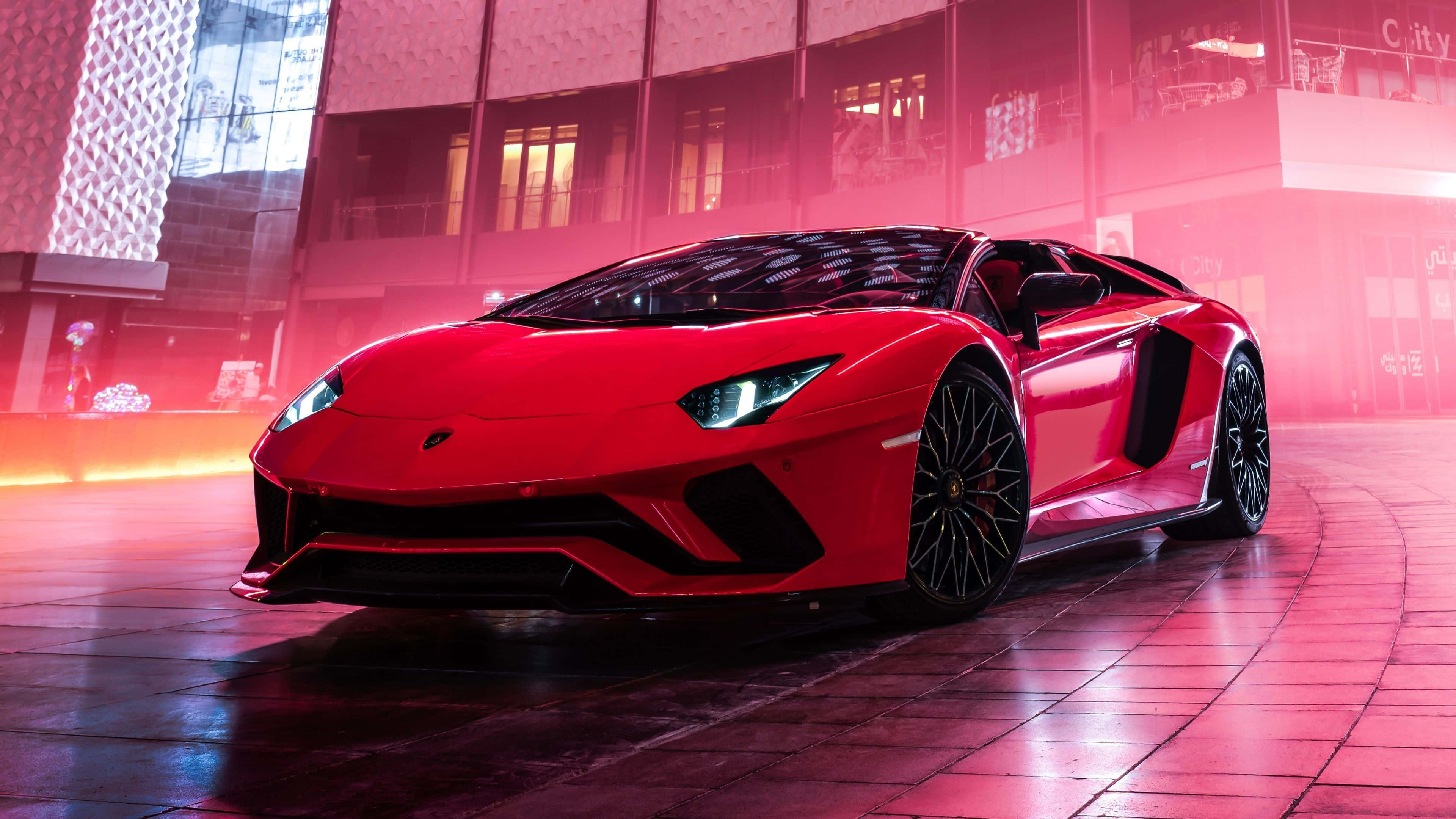 4K 藍寶堅尼 桌布 壁紙 — 一輛鮮紅色的藍寶堅尼 Aventador 在夜間濕潤的城市廣場上，在粉紅色霓虹燈下閃閃發光。