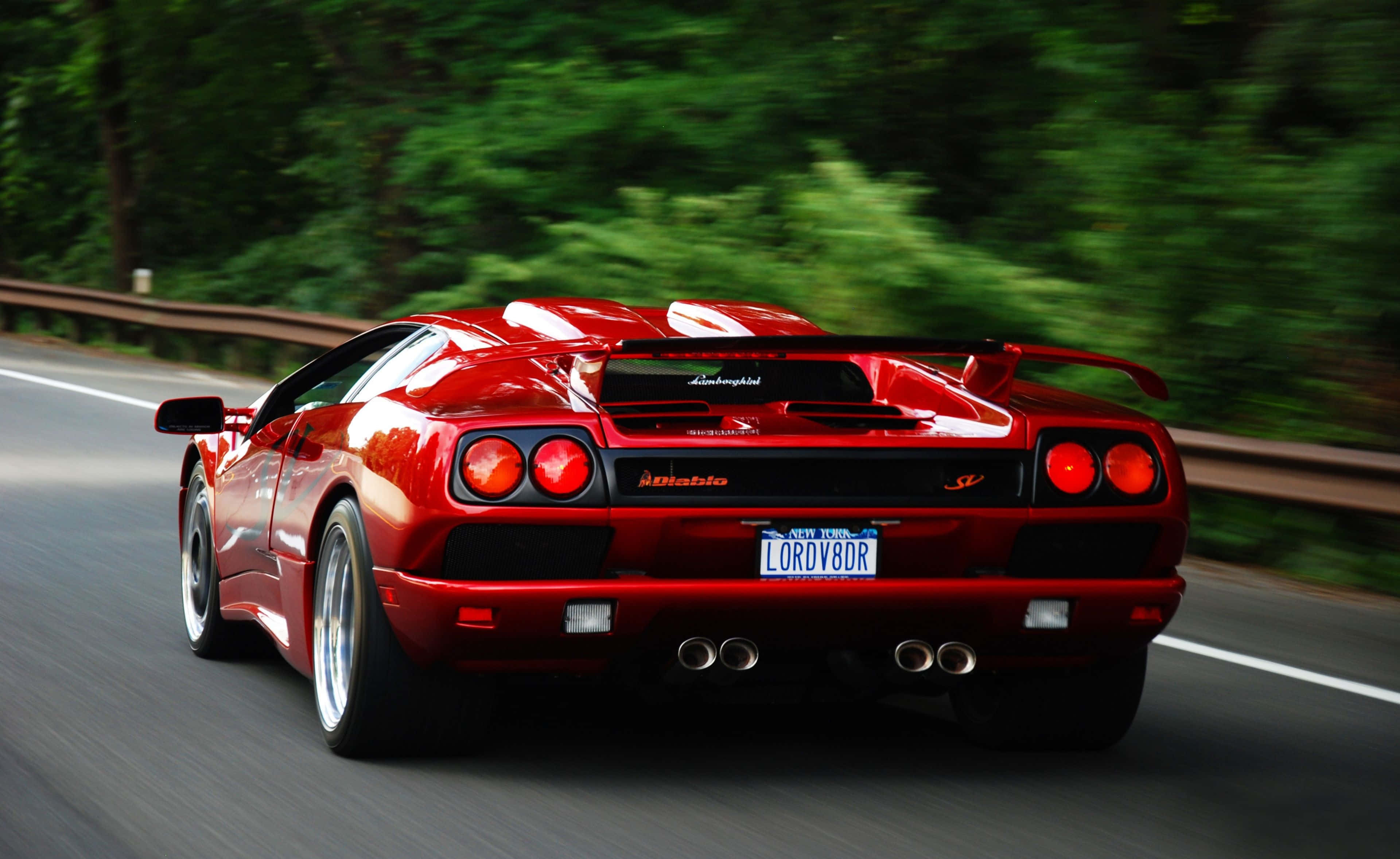 Lamborghini Diablo 桌布 壁紙 — 一輛鮮紅色的藍寶堅尼 Diablo 在森林大道上疾馳，動態模糊效果突顯其力量與流線型設計。