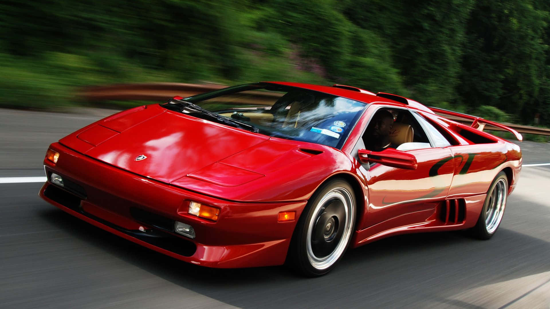 Lamborghini Diablo 桌布 壁紙 — 一輛鮮紅色的藍寶堅尼 Diablo 在蜿蜒的道路上奔馳，背景中茂密的綠樹變得模糊。
