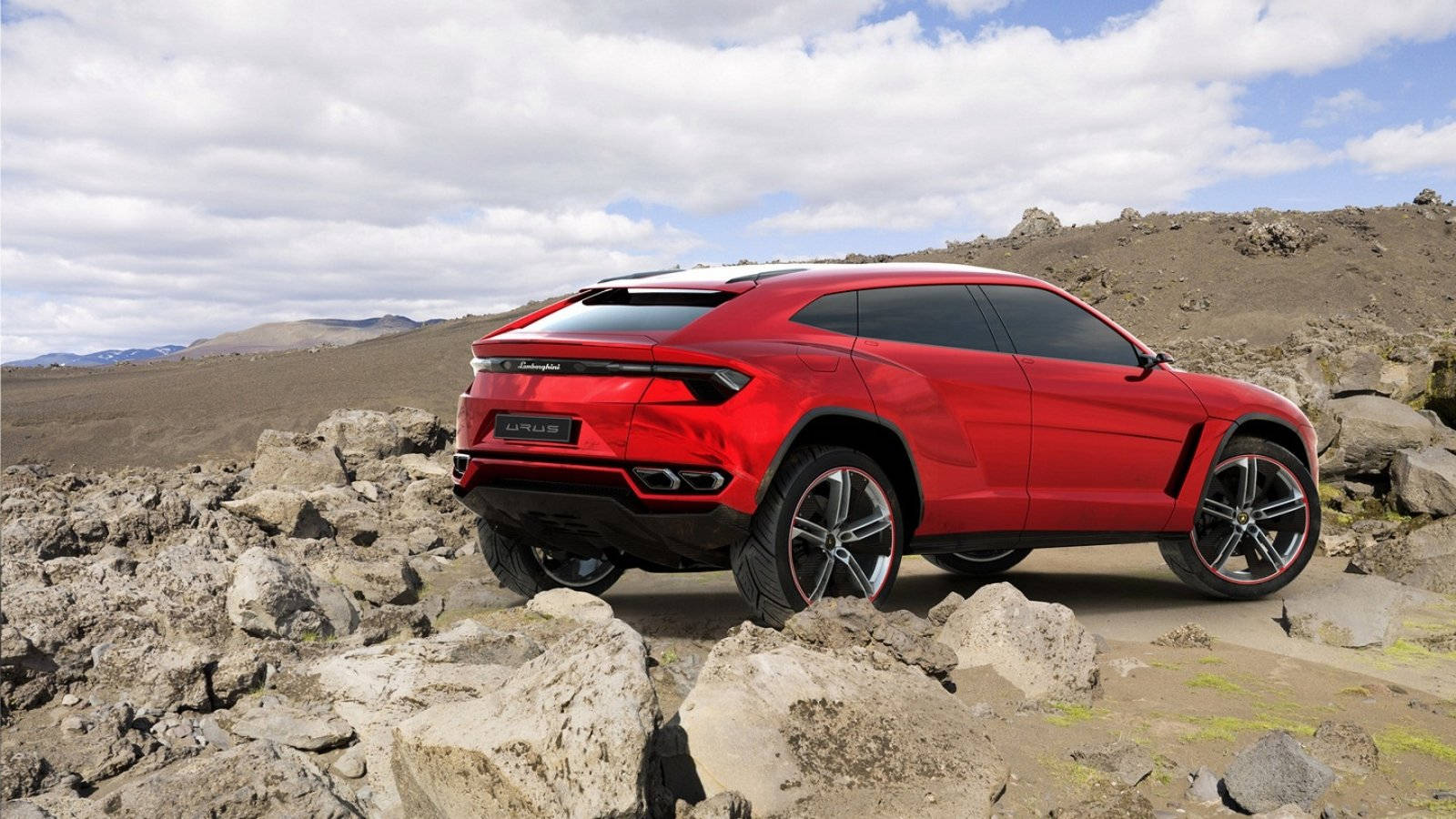 lambo 桌布 壁紙 — 一輛鮮紅色的藍寶堅尼 Urus SUV 在部分多雲的天空下，矗立在崎嶇的火山岩上。