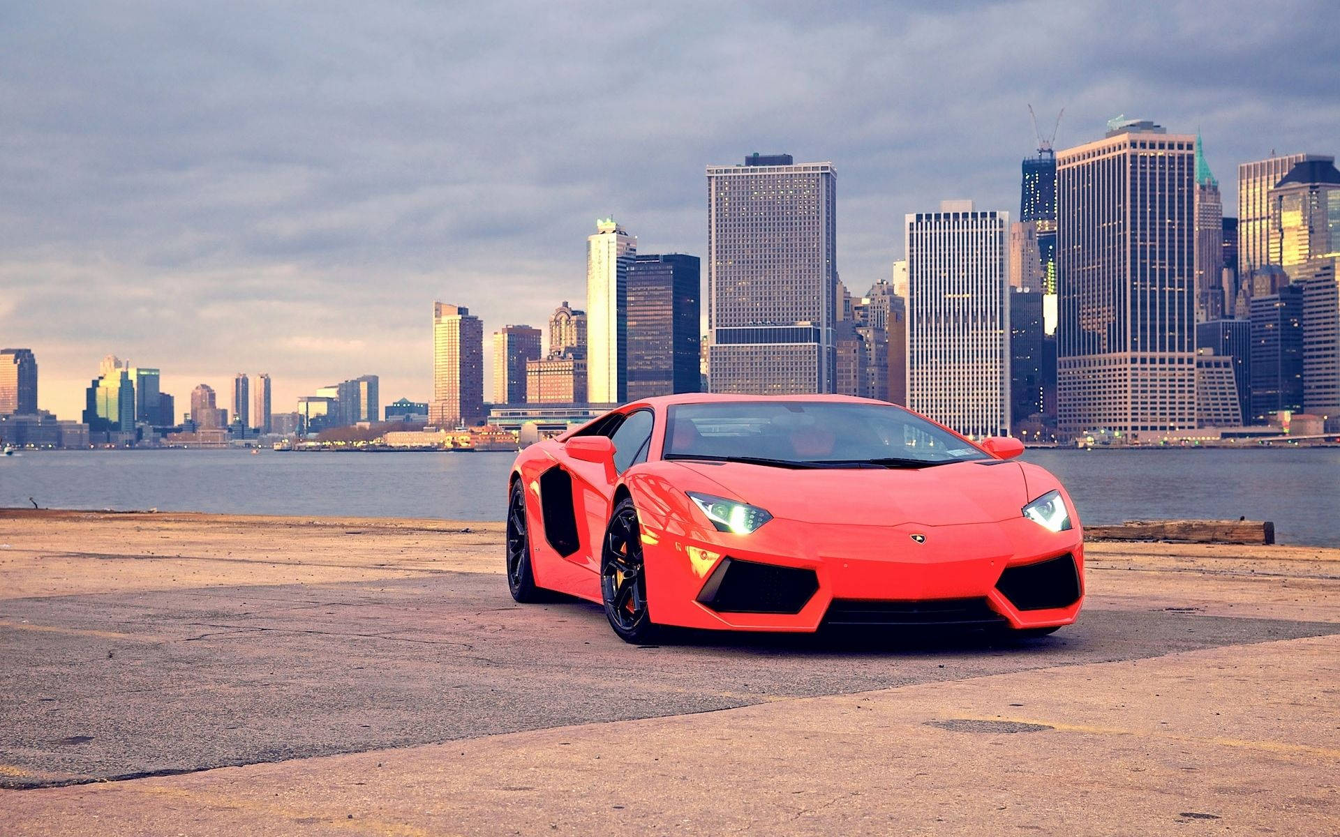 汽車 桌布 壁紙 — 一輛鮮紅色的藍寶堅尼Aventador停泊在海濱碼頭，背景是陰天的城市天際線。