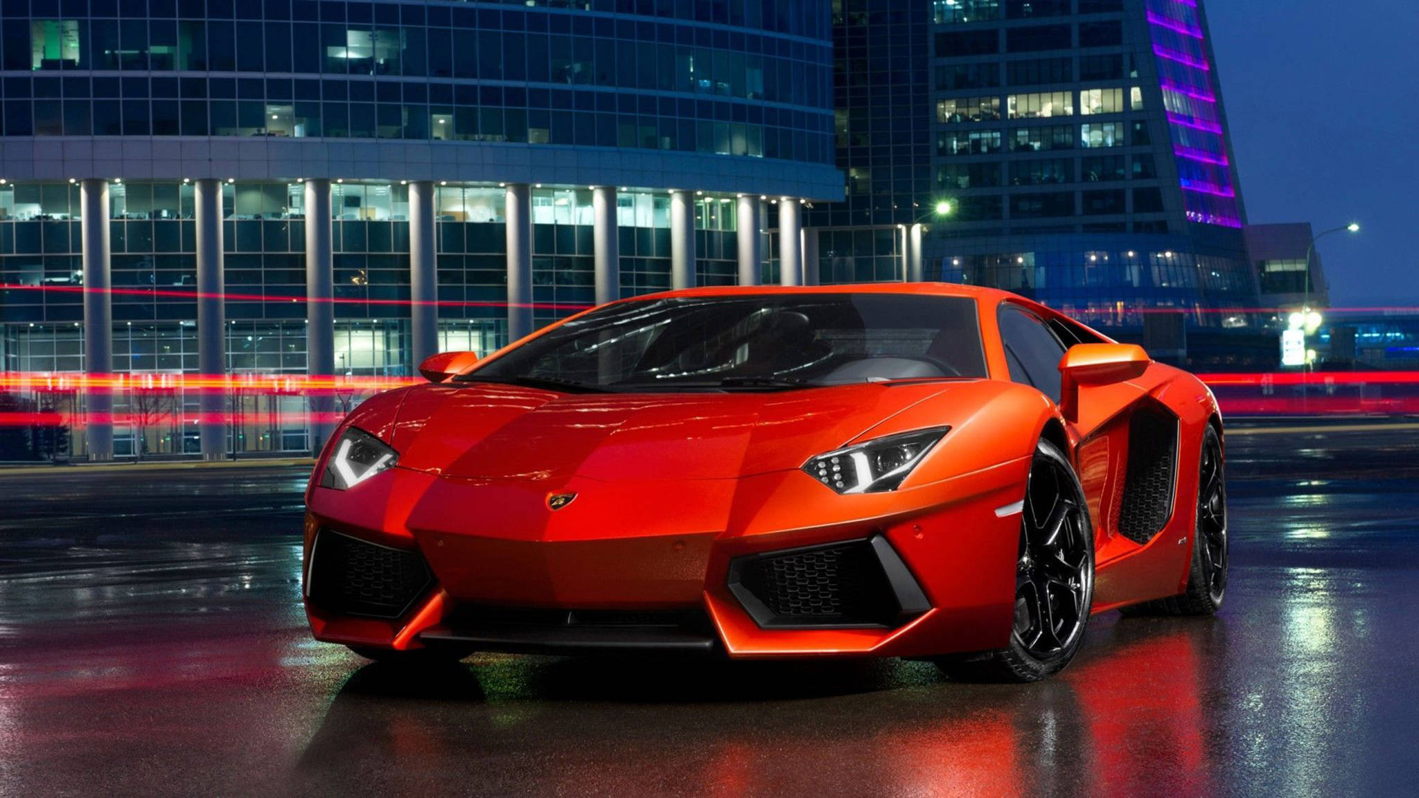 cars 桌布 壁紙 — 一輛鮮紅色的藍寶堅尼Aventador在濕滑的夜街上閃耀著城市燈光，現代玻璃建築後方有模糊的車流線條。