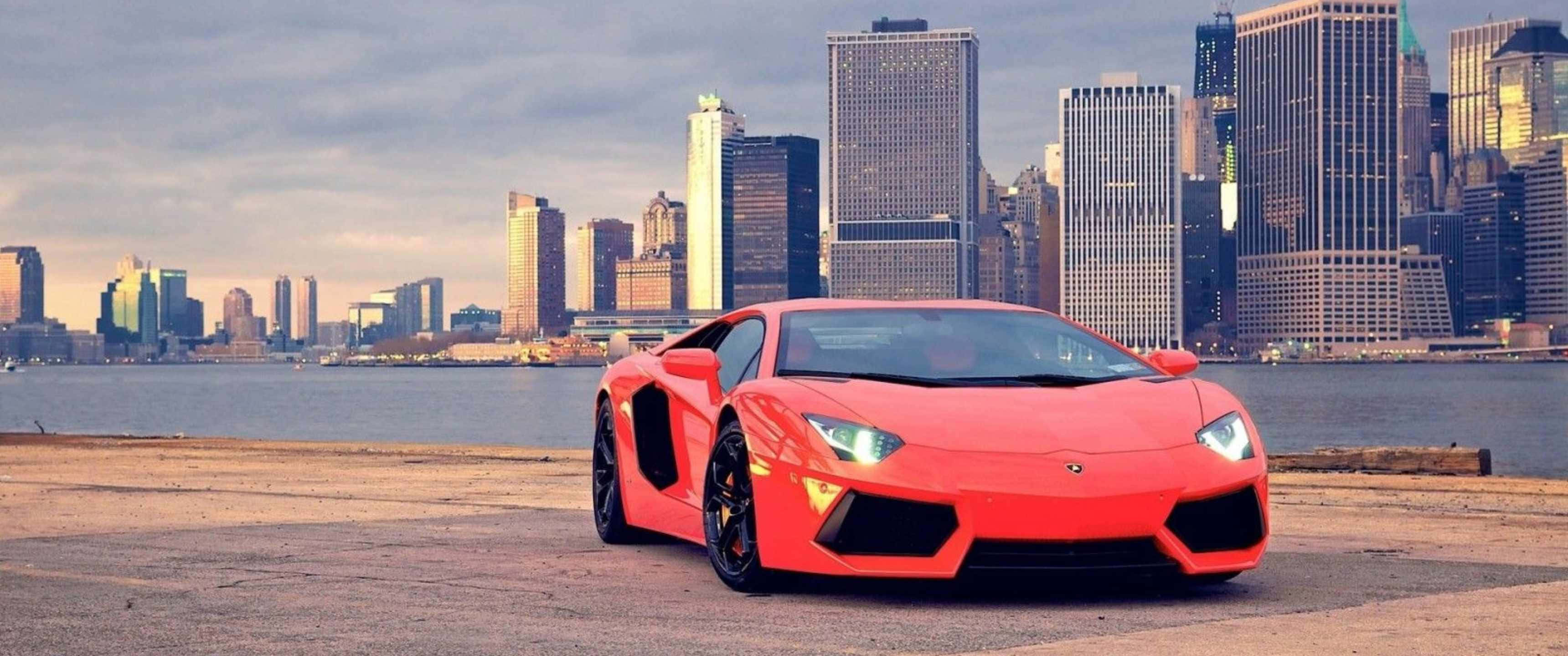 3440x1440p Lamborghini 桌布 壁紙 — 一輛鮮紅色的藍寶堅尼Aventador停泊在海濱碼頭，背景是曼哈頓高聳的天際線。
