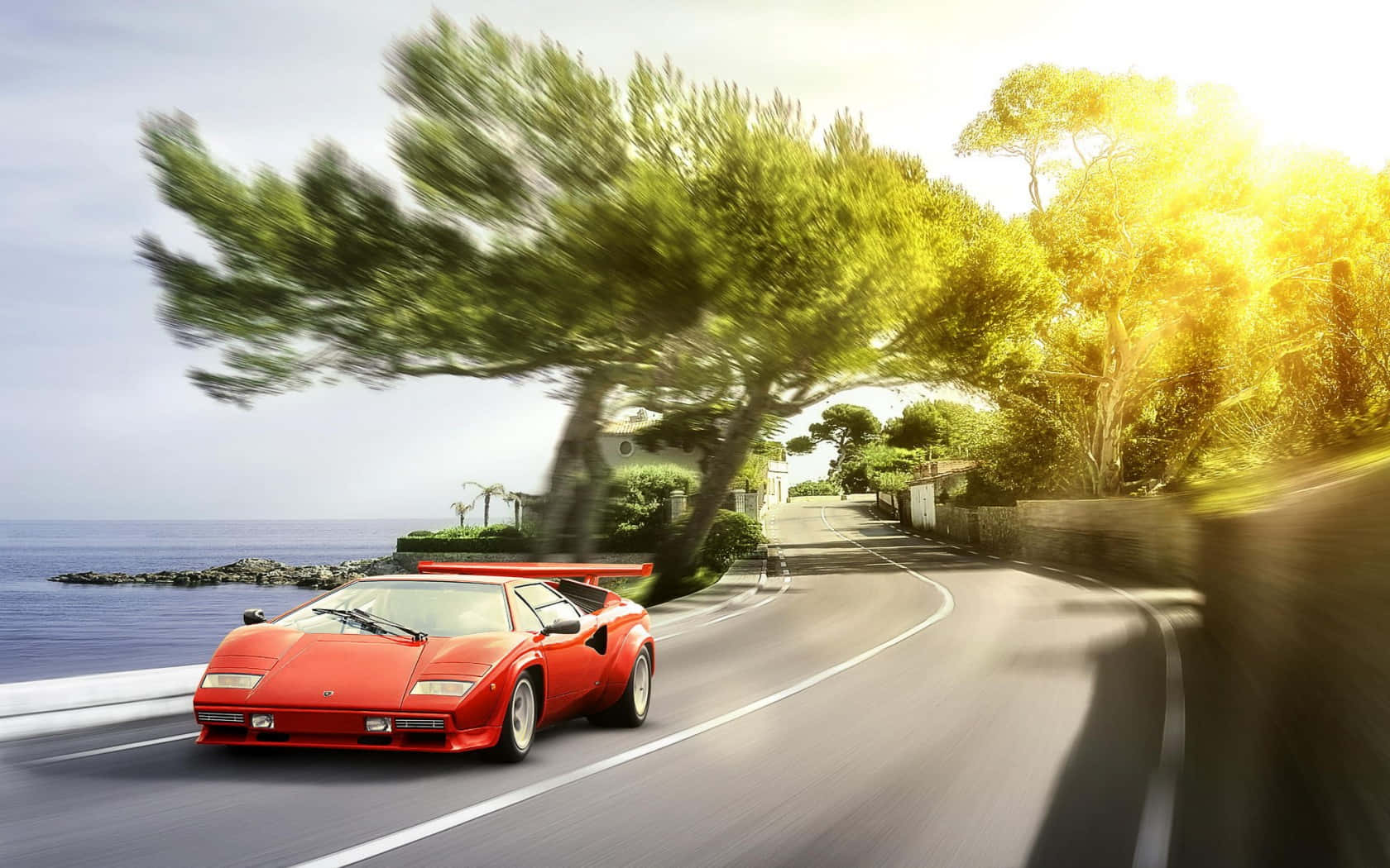 Lamborghini Countach 桌布 壁紙 — 一輛鮮紅色的藍寶堅尼Countach沿著海岸公路疾駛，背景是模糊的樹木和動態的海洋。