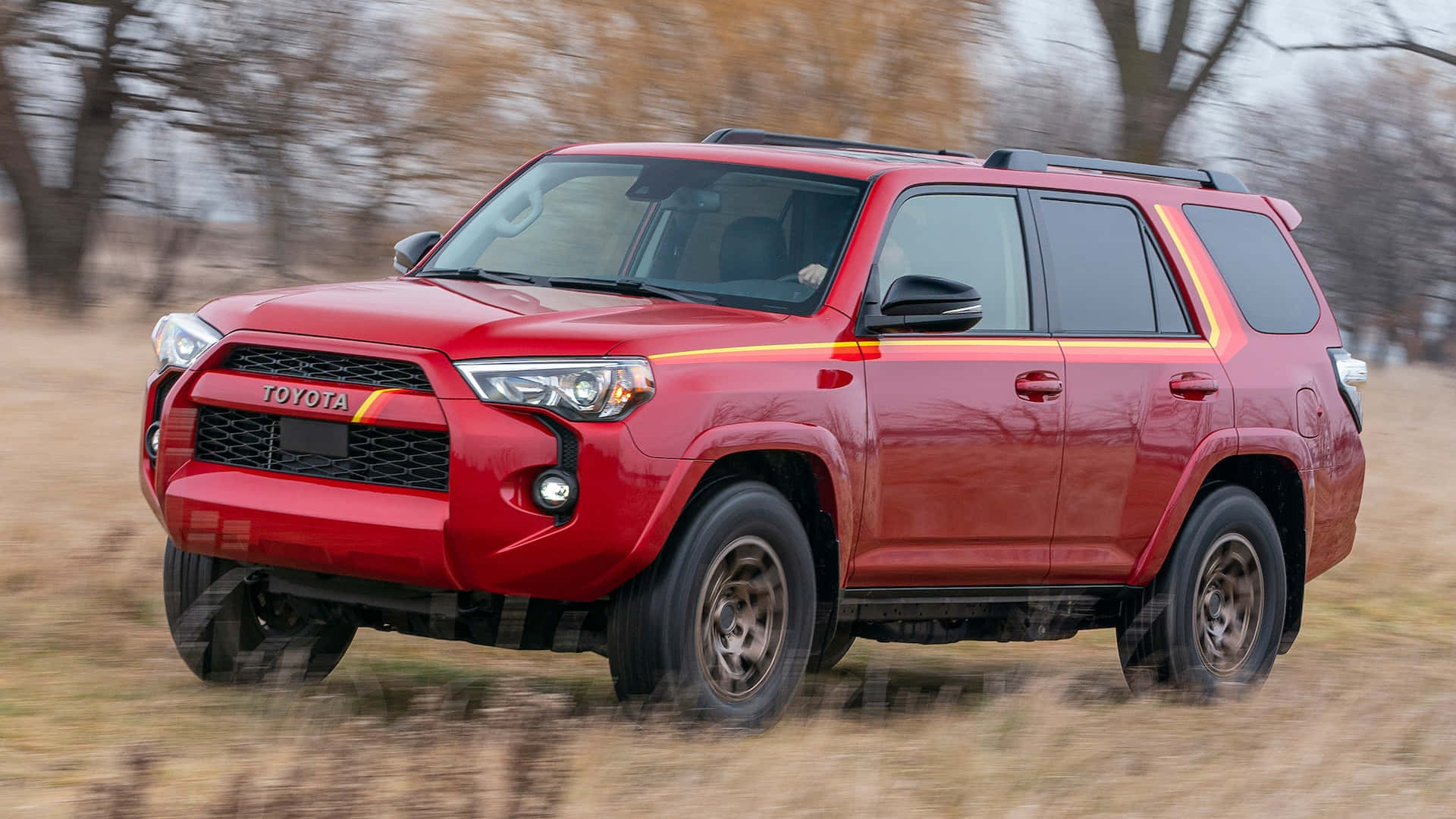 紅色豐田4Runner SUV在草地上行駛，背景有秋樹。 — Toyota Supra Mk4 壁紙