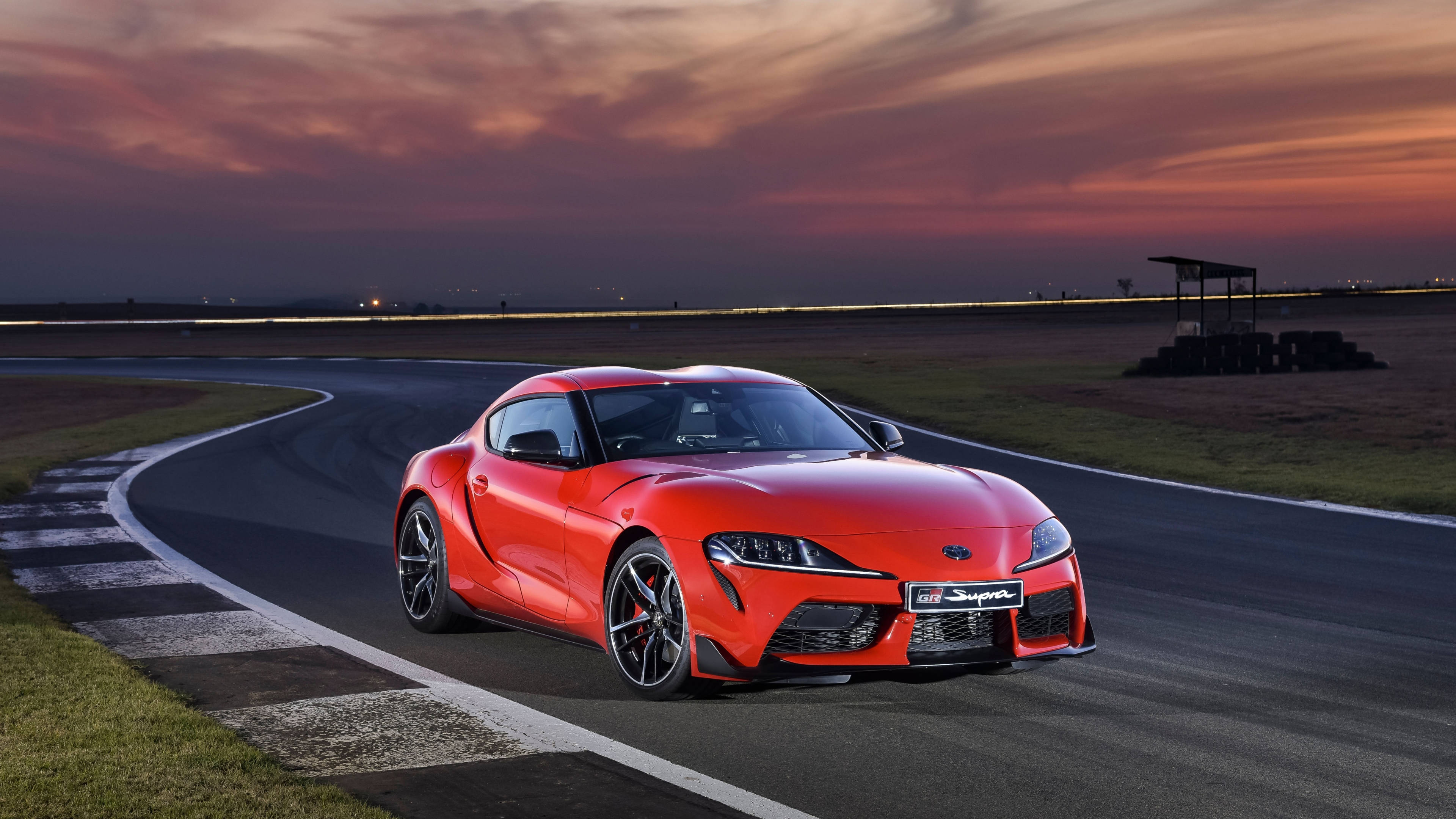 Toyota 桌布 壁紙 — 一輛鮮紅色的豐田Supra在火燒般的夕陽天空下沿著蜿蜒的賽道飛馳。
