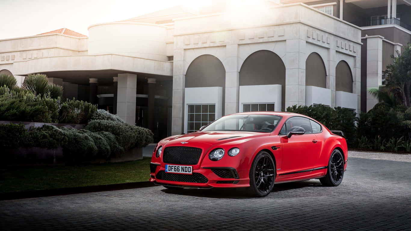 1366x768 Bentley 桌布 壁紙 — 一輛鮮紅色的賓利 Continental GT 停放在石頭車道上，前方是一座帶有拱形柱子的宏偉白色豪宅。