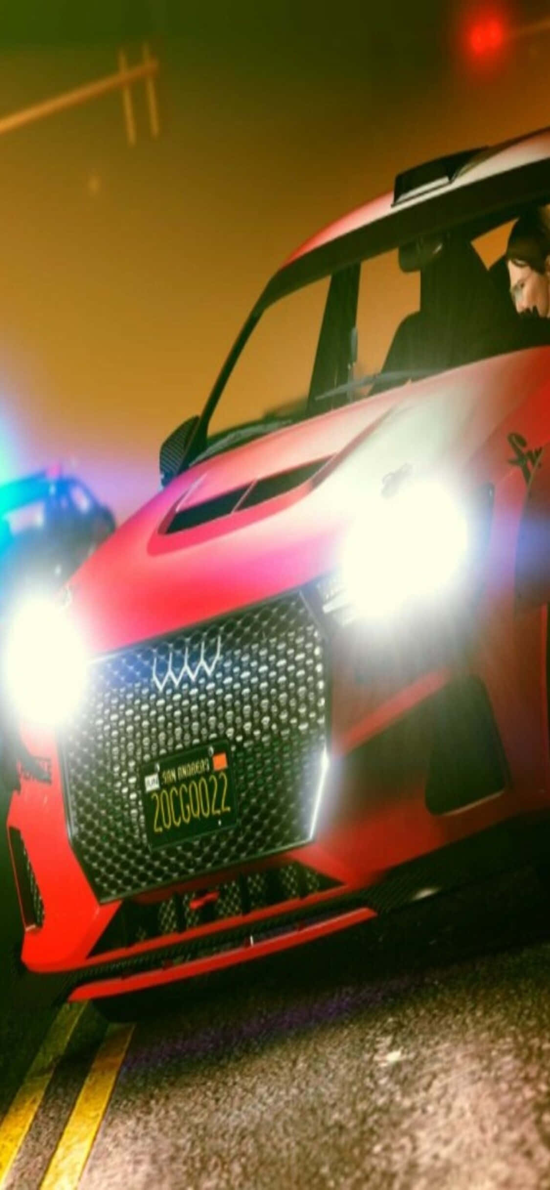 iPhone Xs Dirt Showdown 桌布 壁紙 — 一輛鮮紅色的跑車，車頭燈閃爍，在夜間濕漉漉的城市街道上佔據主導地位，其激進的格柵和流暢的線條反射著霓虹燈光。