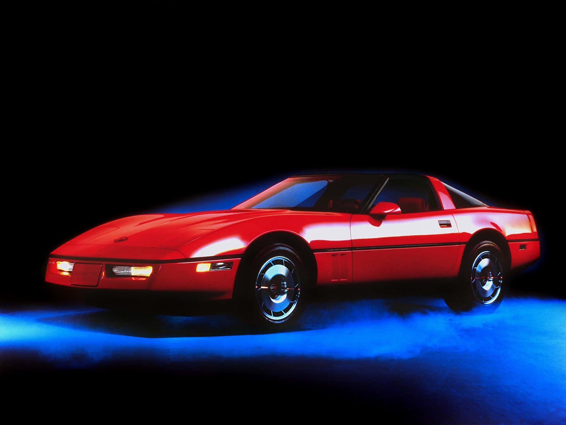 C4 Corvette 桌布 壁紙 — 一輛鮮紅色的跑車在黑色背景上，伴隨著煙霧效果，在戲劇性的藍色燈光下閃耀。