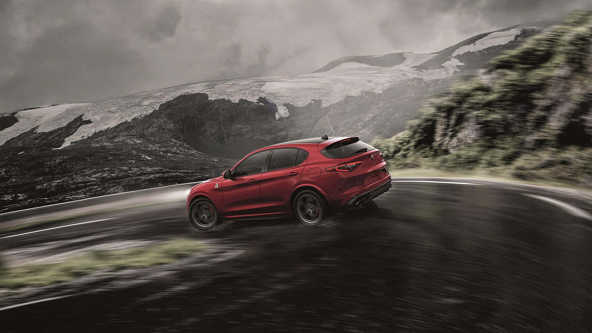 Alfa Romeo Stelvio 桌布 壁紙 — 一輛鮮紅色的跑車沿著蜿蜒的山路疾馳，背景是白雪覆蓋的山峰和暴風雨的天空。