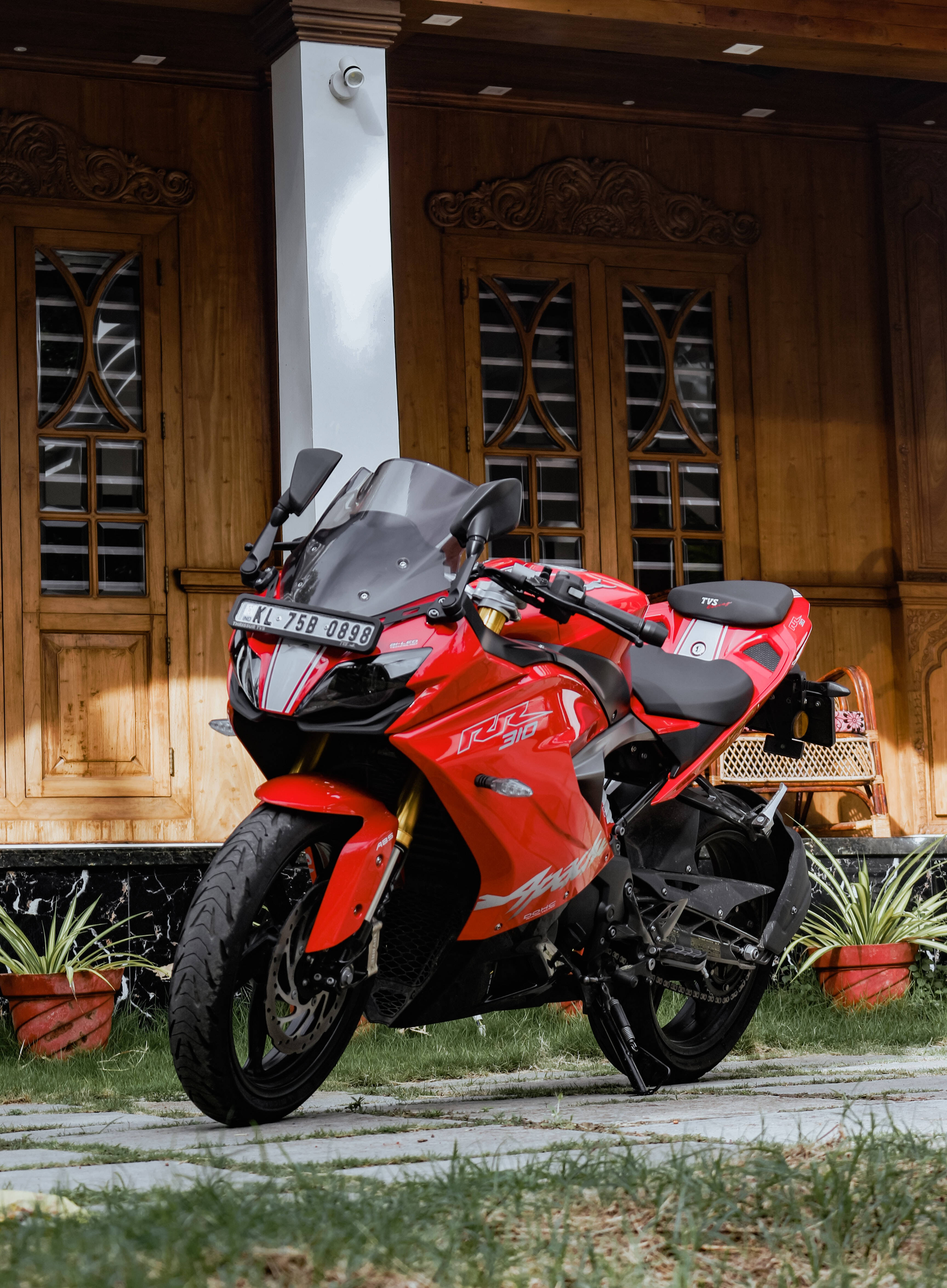 機車 桌布 壁紙 — 一輛鮮紅色的運動機車停放在石徑上，前面是一間有華麗雕刻和盆栽的木屋。