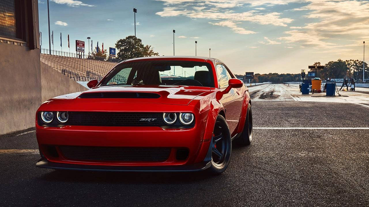 Challenger 桌布 壁紙 — 一輛鮮紅色的道奇挑戰者SRT地獄貓停在賽車場上，夕陽西下，光線戲劇性，天空晴朗。