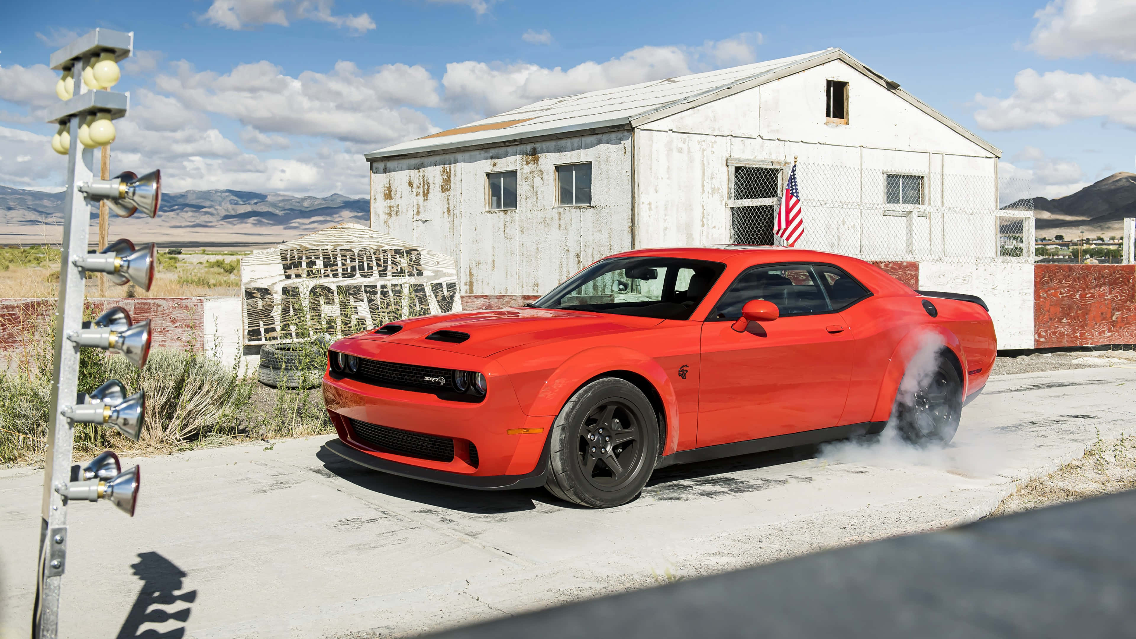 桌布 壁紙 — 一輛鮮紅色的道奇挑戰者在晴朗的藍天下，在風化的「Wendover Raceway」標誌前燒胎。