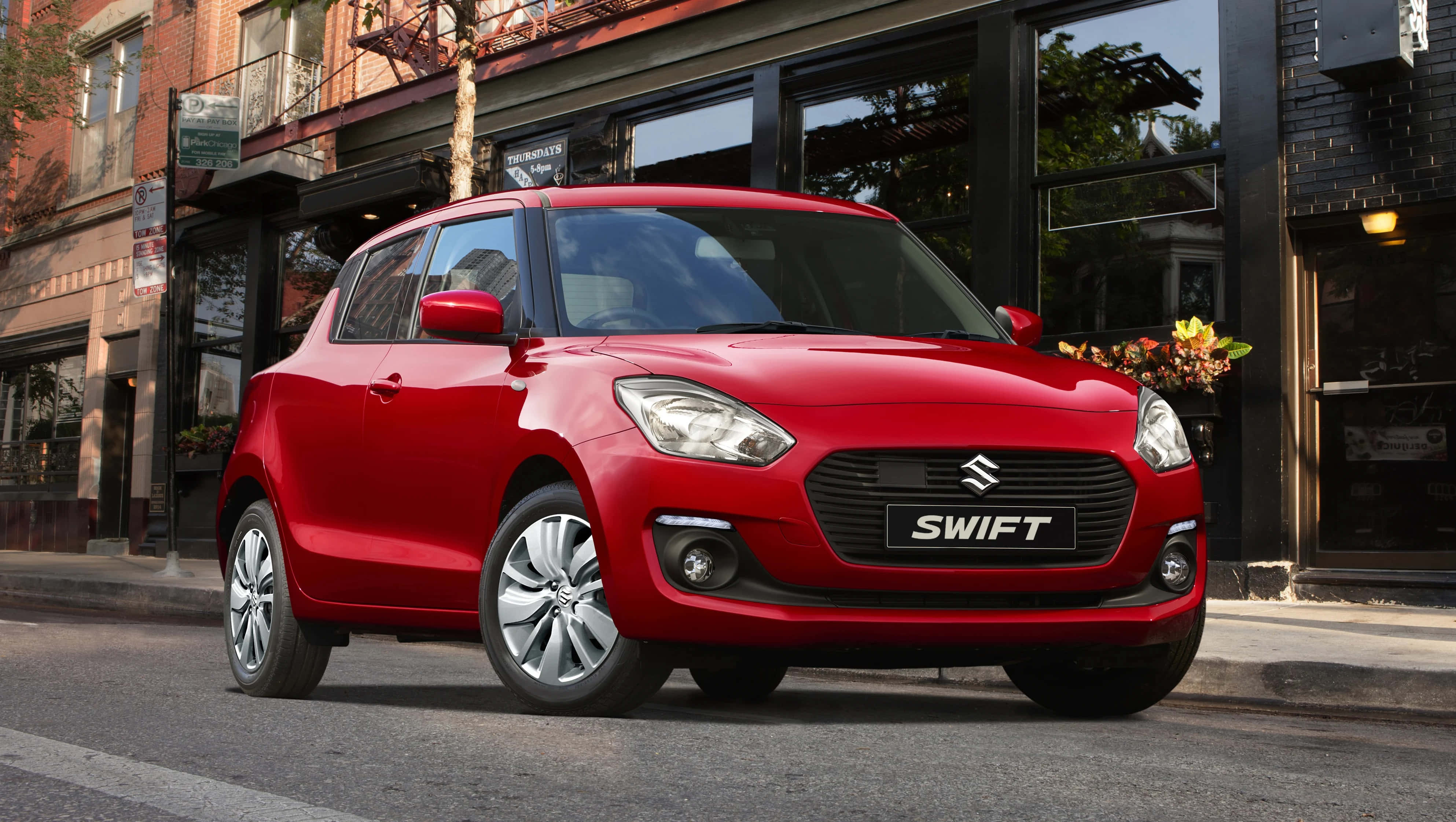 Compact Car 桌布 壁紙 — 一輛鮮紅色的鈴木 Swift 停放在城市的街道上，背景是磚造建築和商店門面。