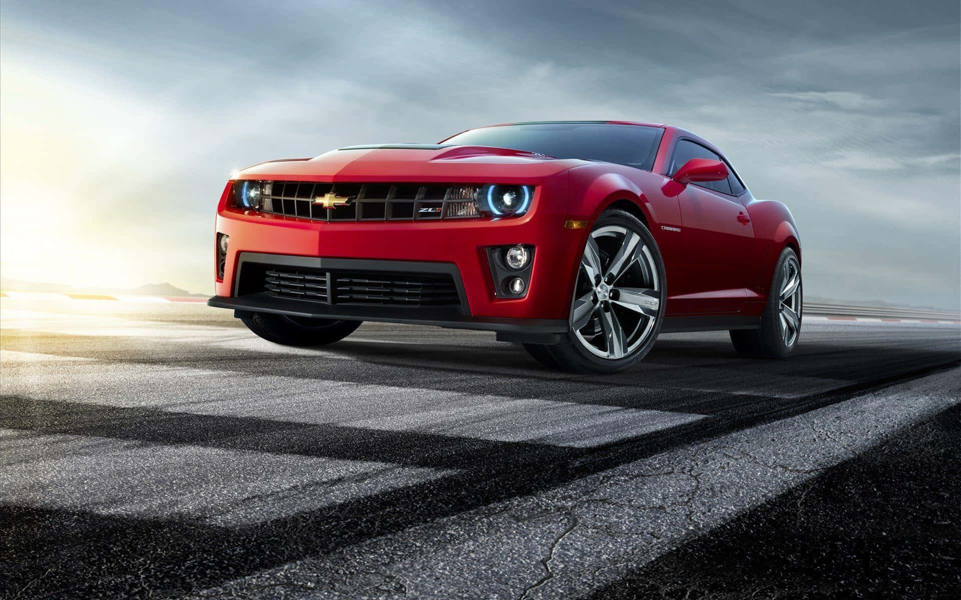 Cool Camaro 桌布 壁紙 — 一輛鮮紅色的雪佛蘭 Camaro SS 在佈滿裂痕的瀝青路上疾馳，背景是戲劇性的多雲天空，陽光四射。