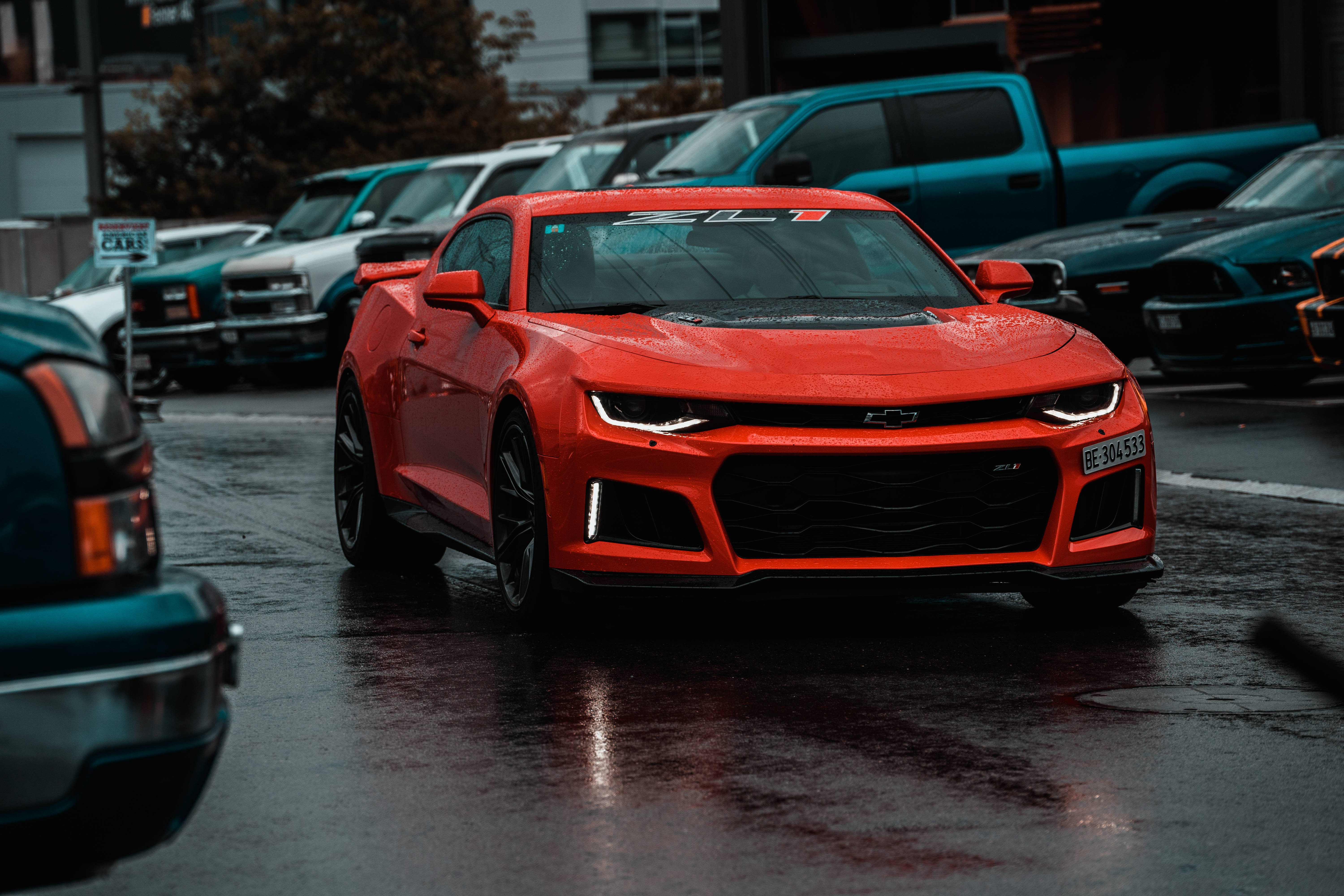 Chevrolet 桌布 壁紙 — 一輛鮮紅色的雪佛蘭Camaro ZL1在潮濕的停車場上閃閃發光，天空多雲，倒影在瀝青上閃爍。