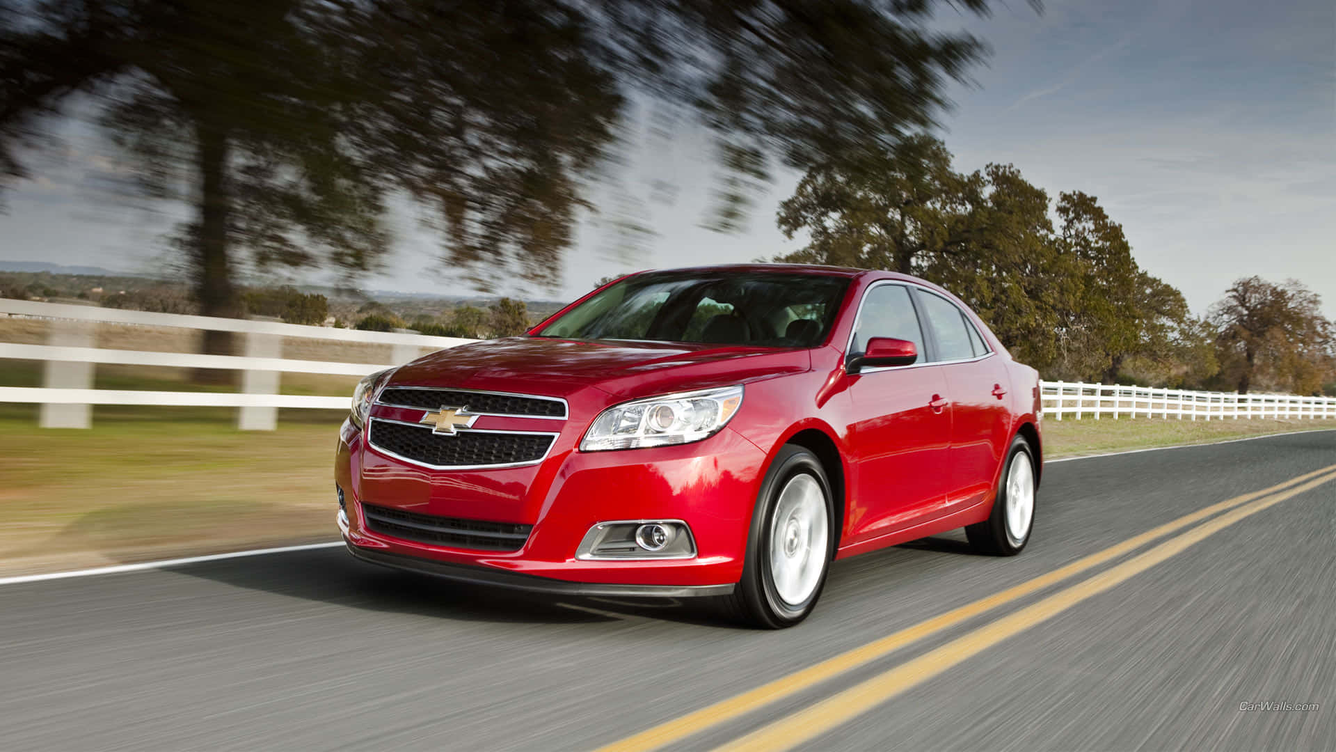 Chevy Malibu 桌布 壁紙 — 一輛鮮紅色的雪佛蘭轎車在鄉村道路上飛馳，背景有模糊的樹木和白色圍欄。