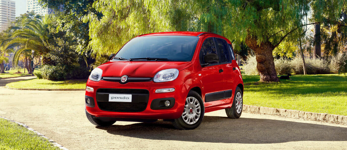 Fiat Panda 桌布 壁紙 — 一輛鮮紅色的飛雅特 Panda 停放在陽光普照的鋪砌小徑上，旁邊是茂密的綠草和枝葉繁茂的樹木。