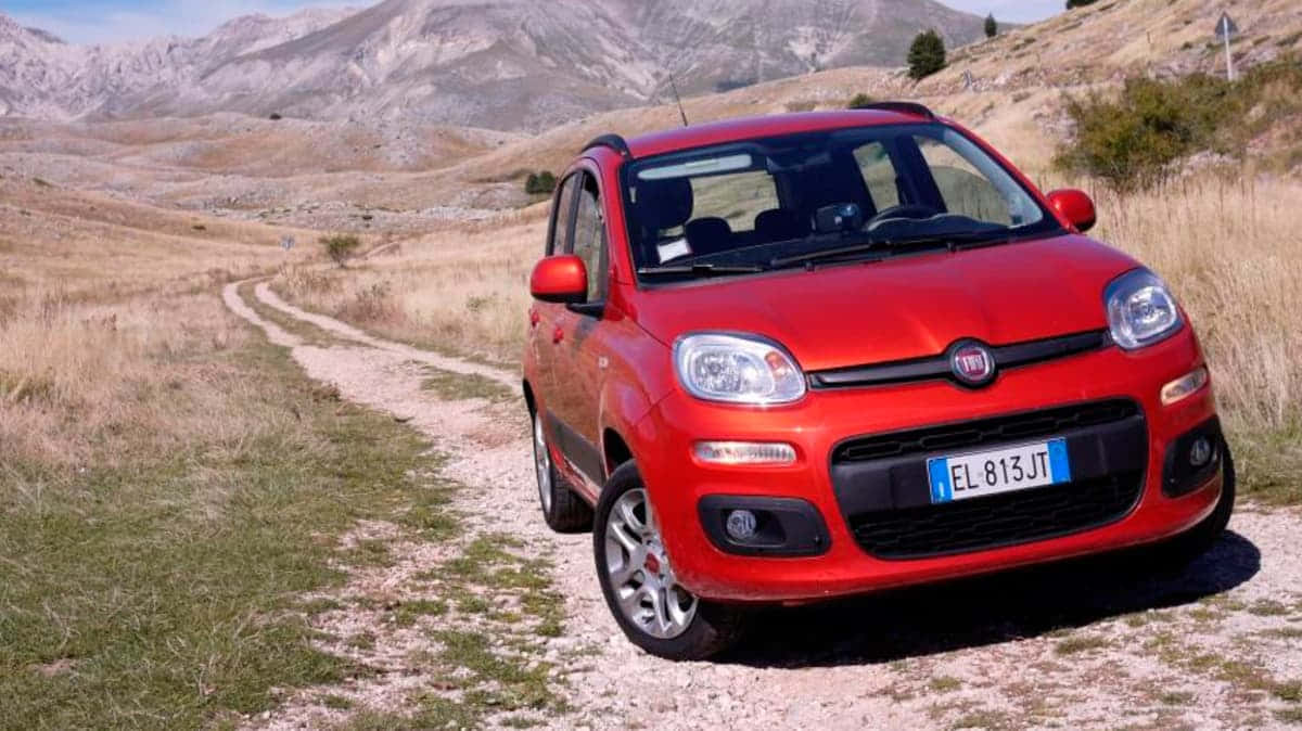 Fiat Panda 桌布 壁紙 — 一輛鮮紅色的飛雅特 Panda 停放在蜿蜒的泥土路上，穿越乾燥的草原，背景是崎嶇的山脈。