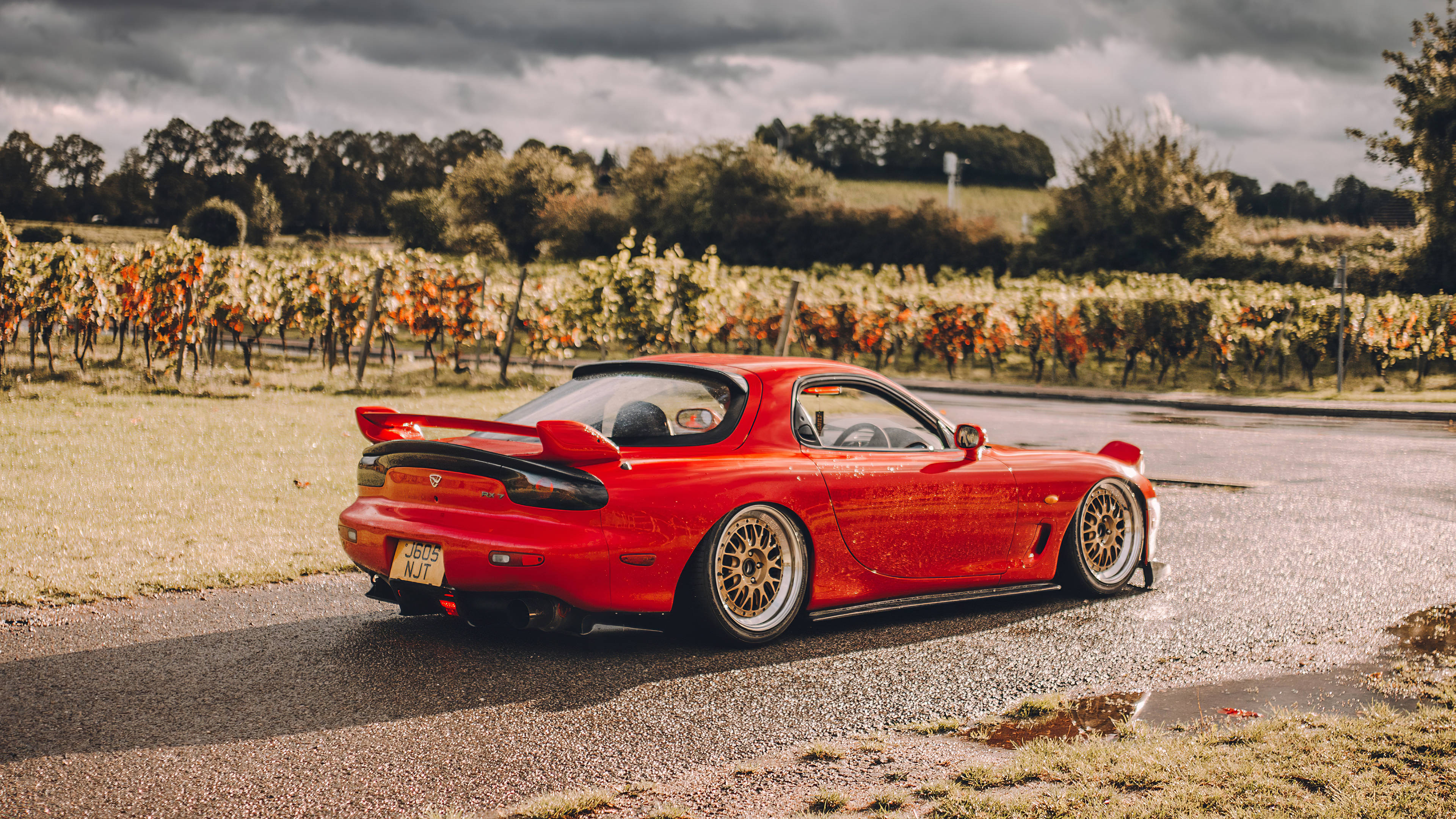 Mazda 桌布 壁紙 — 一輛鮮紅色的馬自達RX-7跑車停在潮濕的道路上，旁邊是秋天的葡萄園，天空多雲。