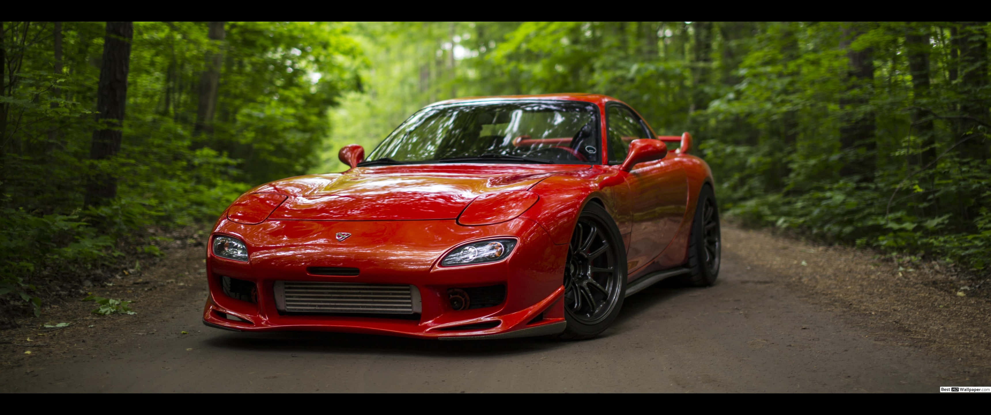 3440x1440p Ferrari 桌布 壁紙 — 一輛鮮紅色的馬自達RX-7跑車在森林泥路上閃閃發光，周圍是茂密的綠樹。
