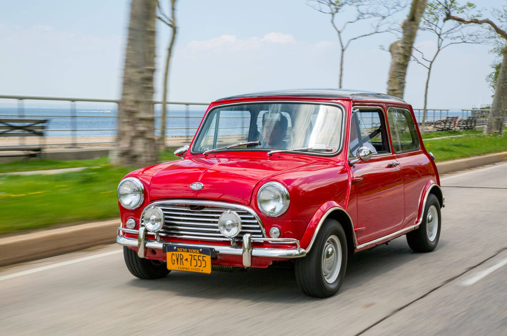 driving 桌布 壁紙 — 一輛鮮紅色經典Mini Cooper沿著海岸道路行駛，背景有模糊的樹木和海洋。